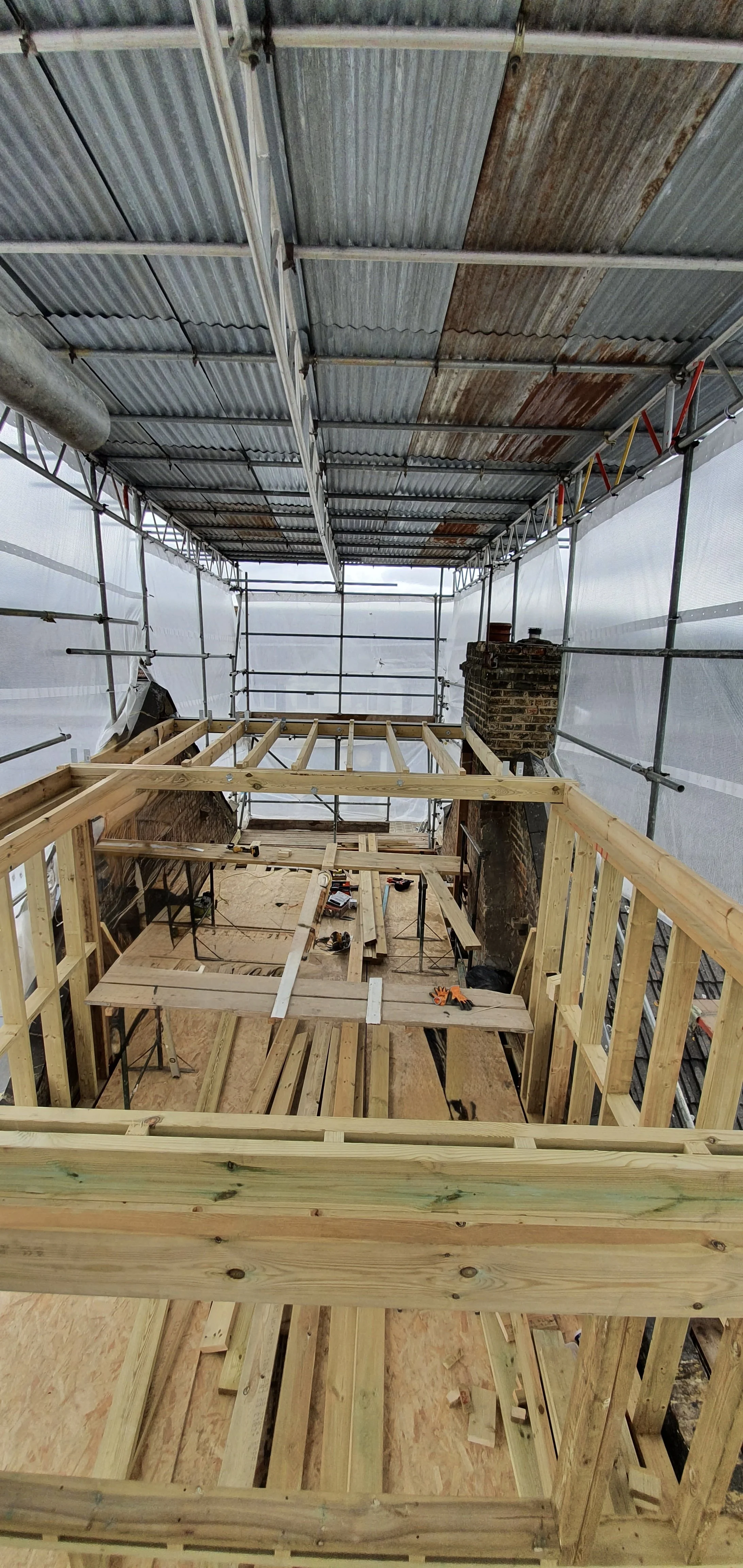 Wooden framing for a construction project inside scaffolding with metal roofing and a brick fireplace.