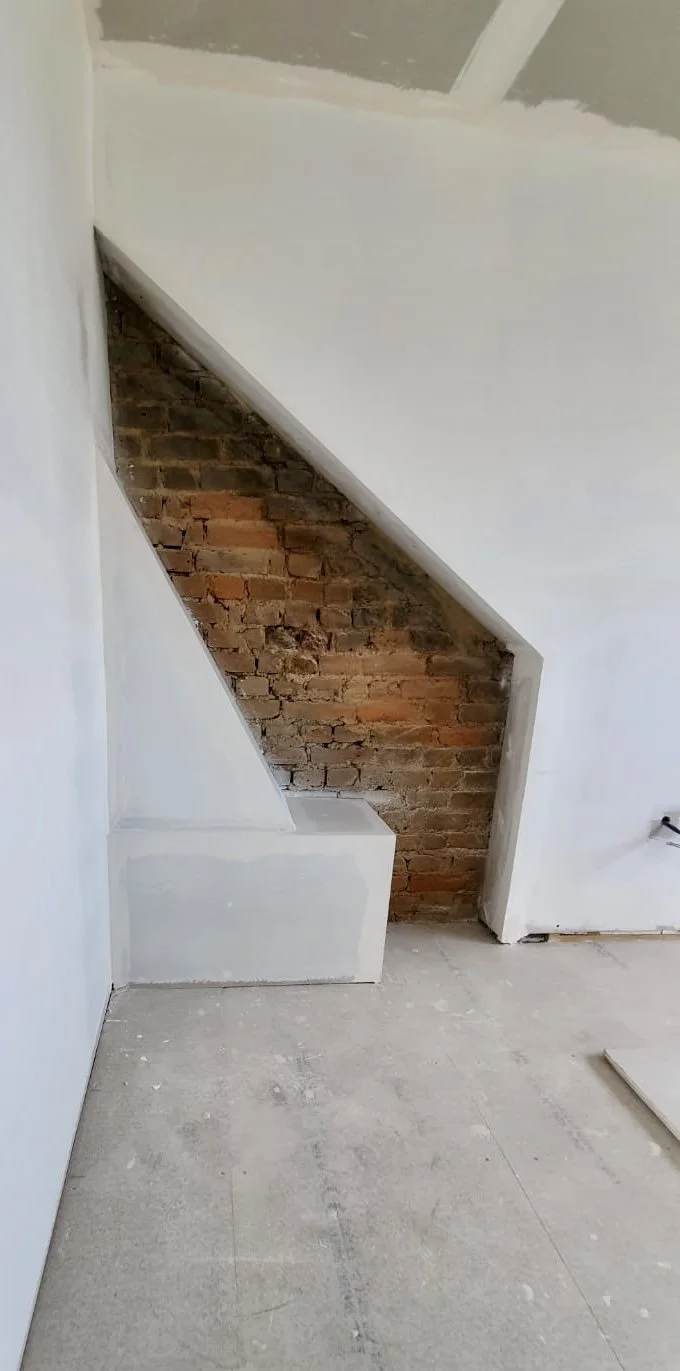 Interior wall with exposed brick under a diagonal cut in the plaster, showing unfinished construction.