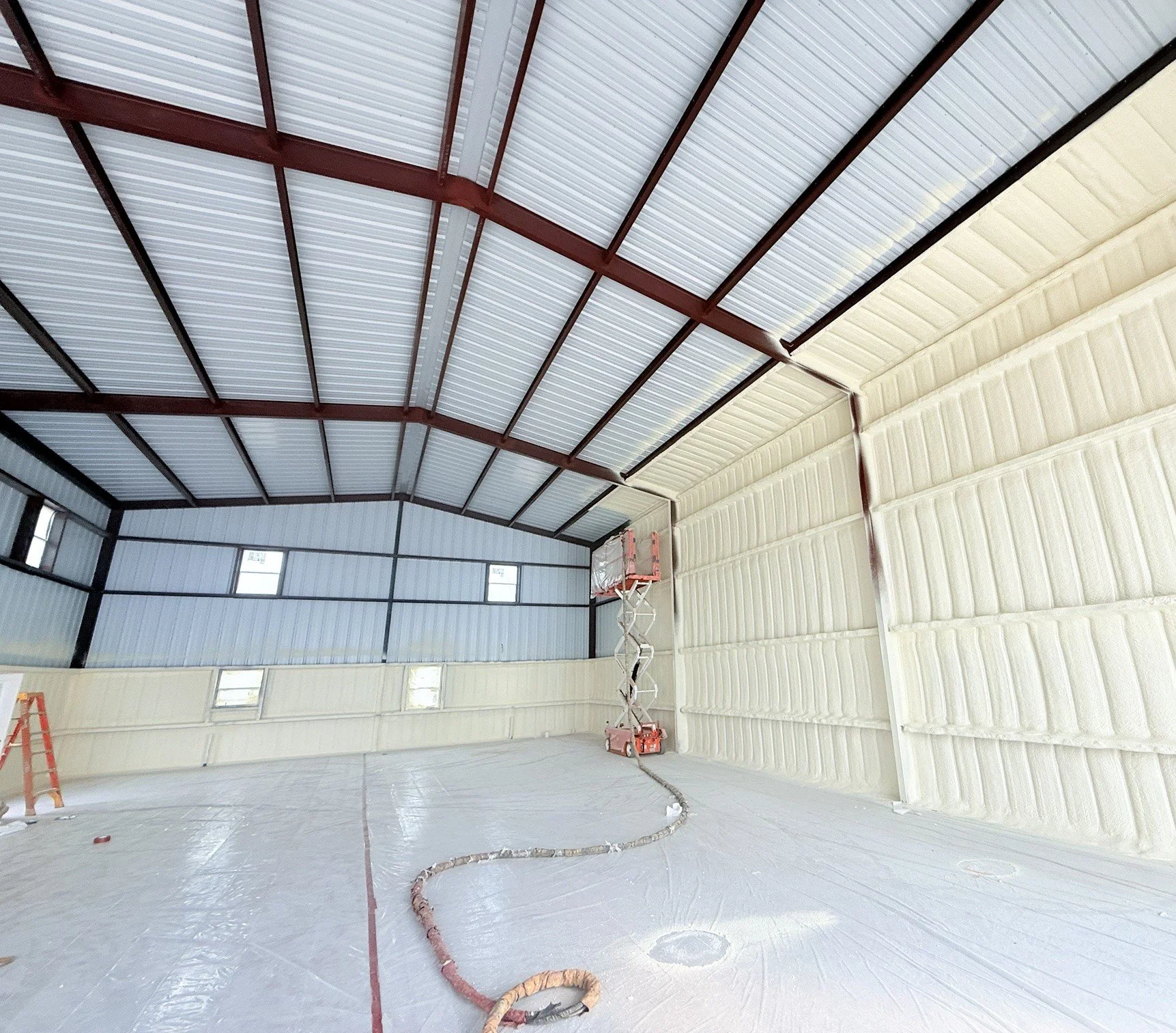 Spray foam being applied to the wall panels of a red iron steel building