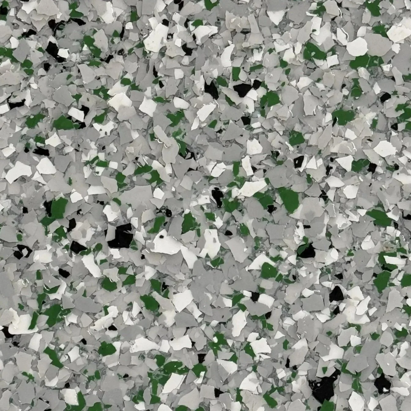 Close-up of a surface covered in multi-colored confetti, predominantly gray, with some green, black, and white pieces.