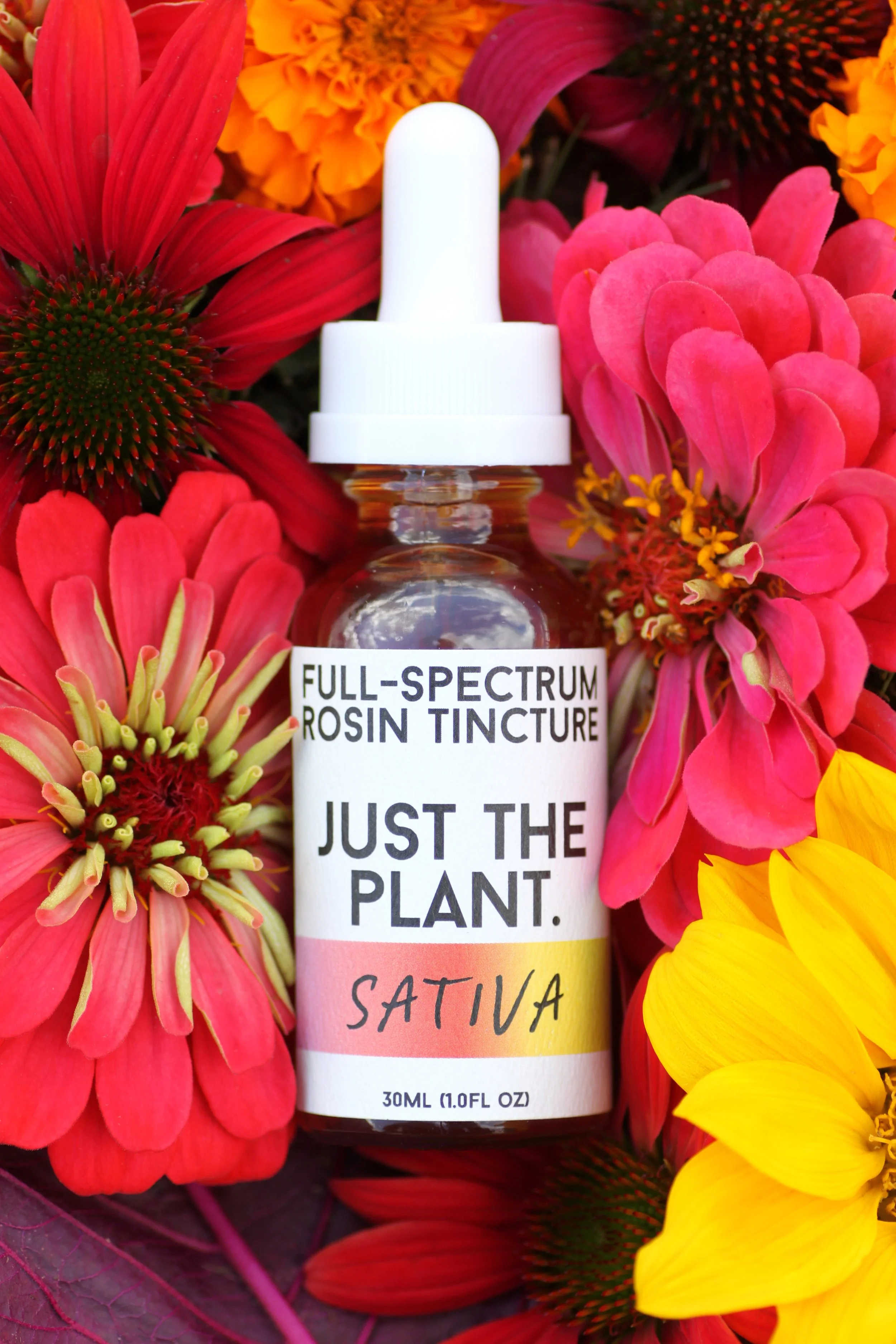 A bottle of Full Spectrum Rosin Tincture labeled "Just the Plant. Sativa" surrounded by colorful flowers including pink, red, and yellow blossoms.