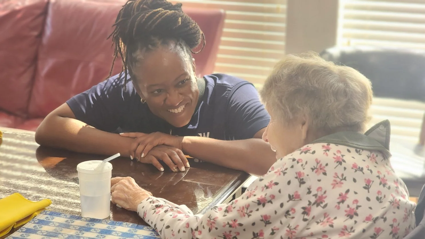 Care That Connects: Kim smiles while engaging one-on-one with a resident during a calm, meaningful activity—showcasing compassion, comfort, and community support.