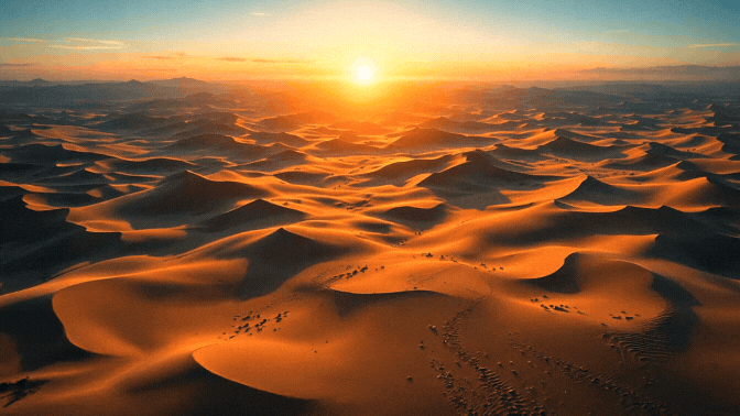 Sunset over vast sand dunes in a desert landscape.