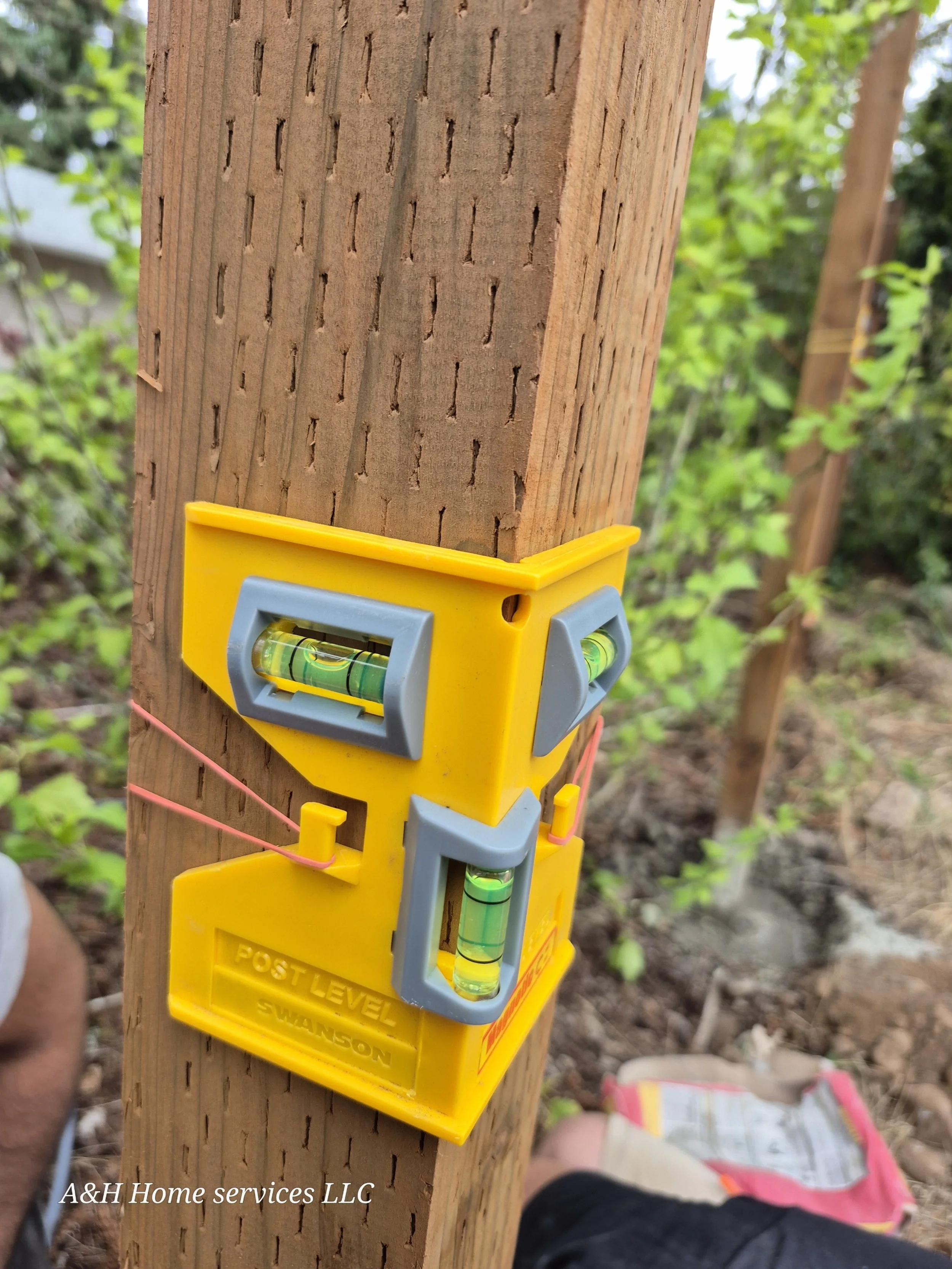 Using a yellow post level to check the level of a wooden post in an outdoor setting.