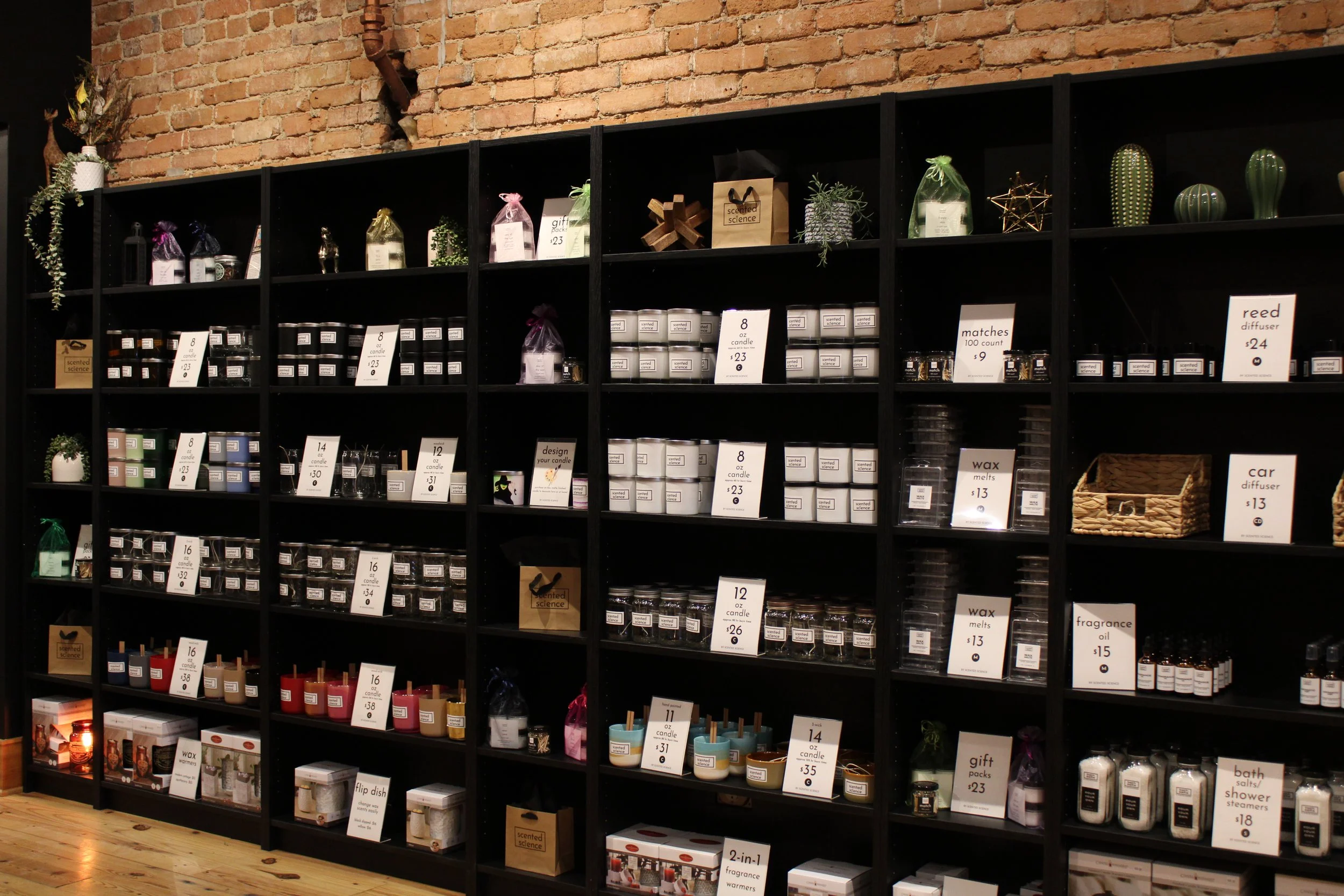 Black shelves filled with candles, wax melts, diffusers, and gift sets in a store with exposed brick wall.