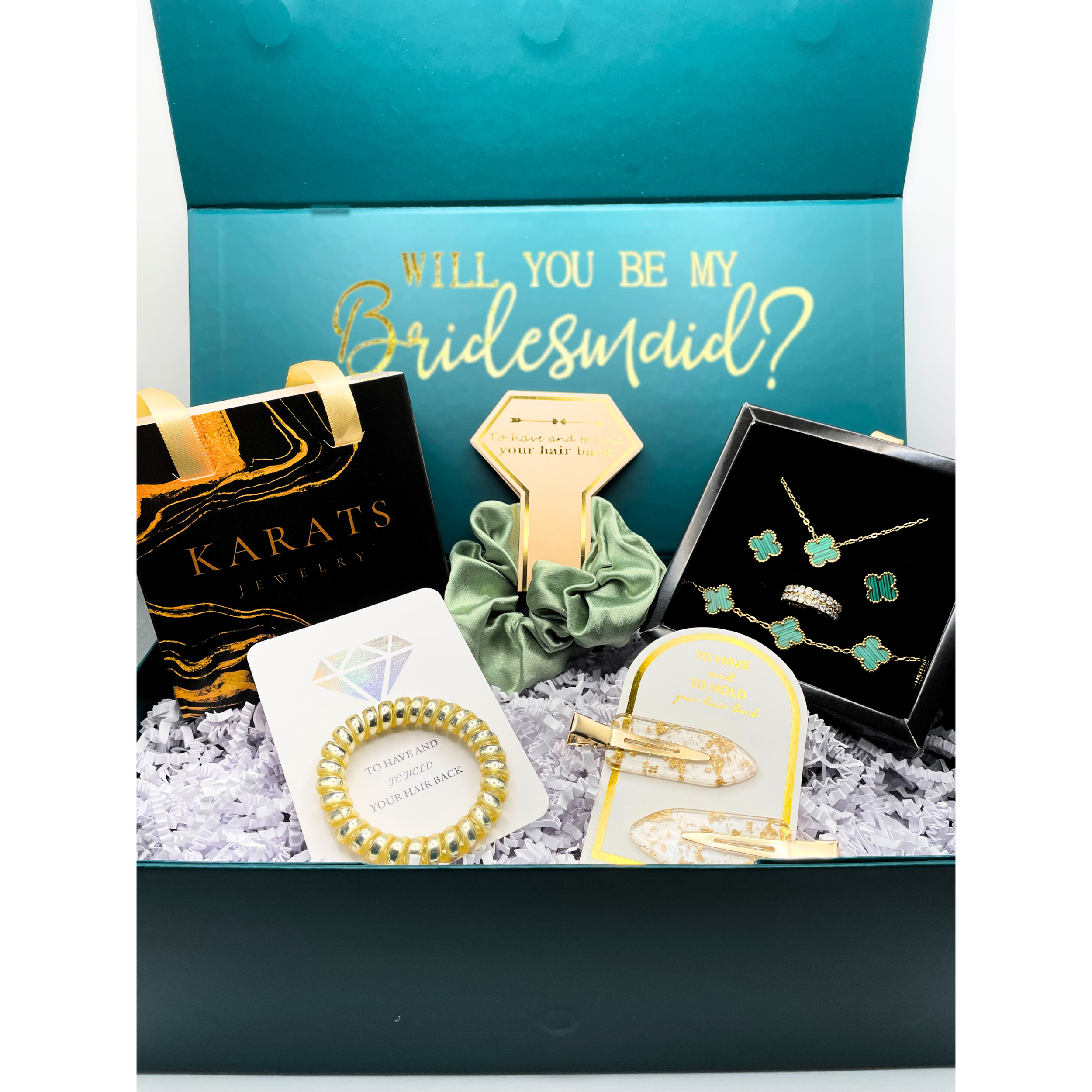 A gift box contains jewelry and hair accessories, with a blue interior that has gold lettering asking, 'Will you be my Bridesmaid?'