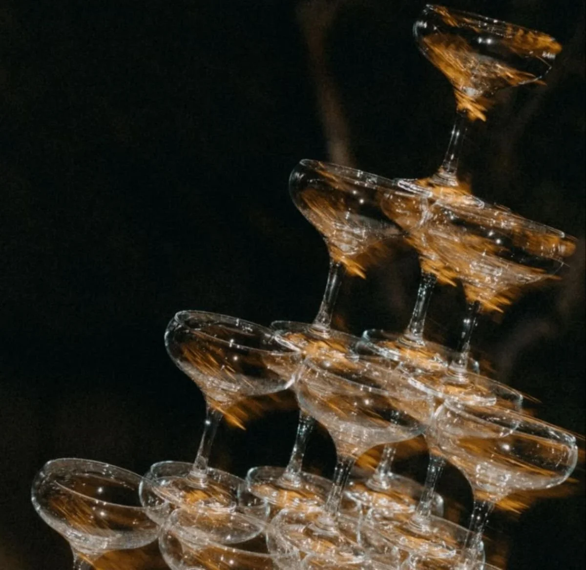 A pyramid of stacked empty martini glasses with reflections and a black background.