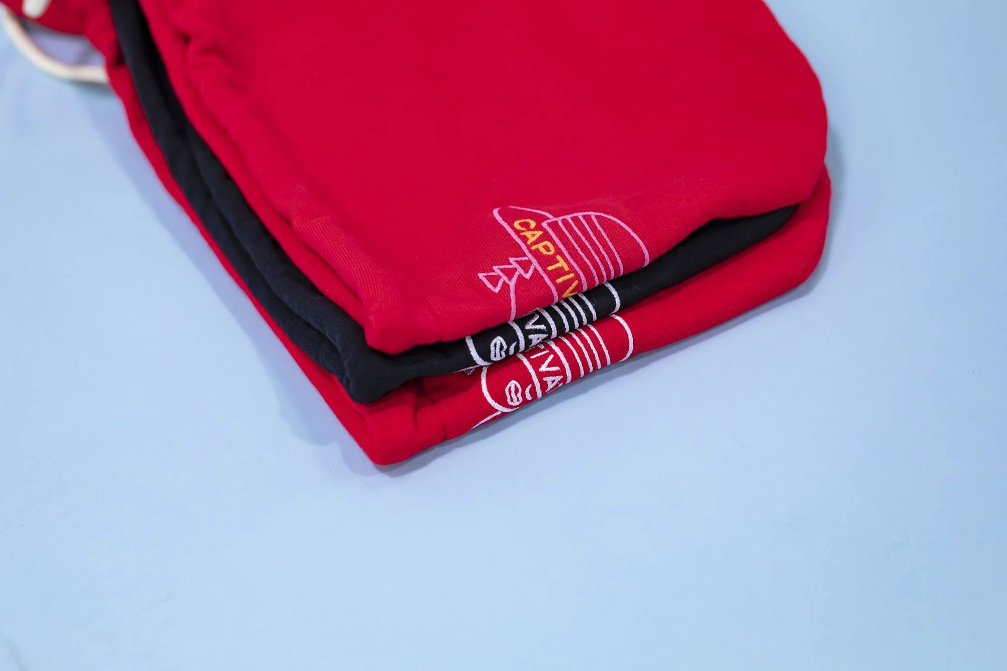 Stacked red, black, and possibly gray or white apparel, with visible graphic or text, on a light blue surface.