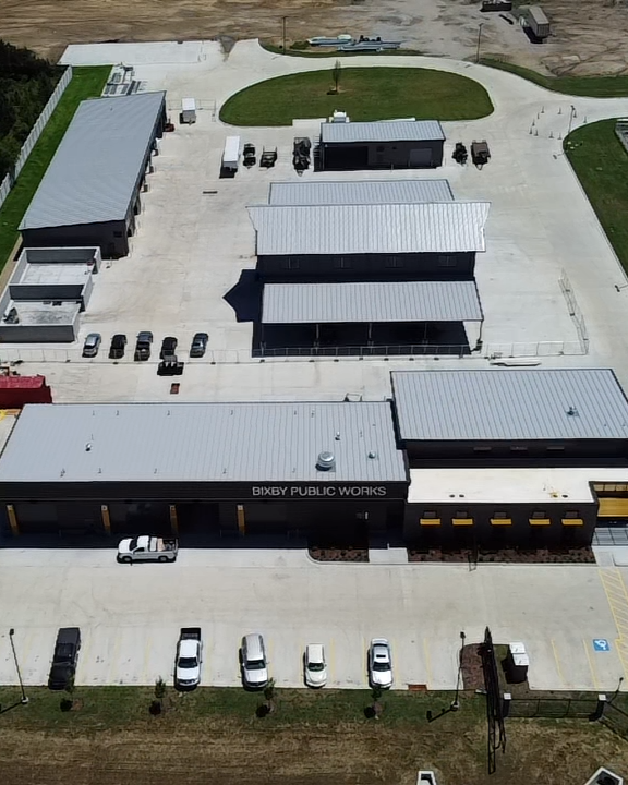 Aerial view of Bixby Public Works building with parking lot and surrounding structures, including a small grassy area at the back.