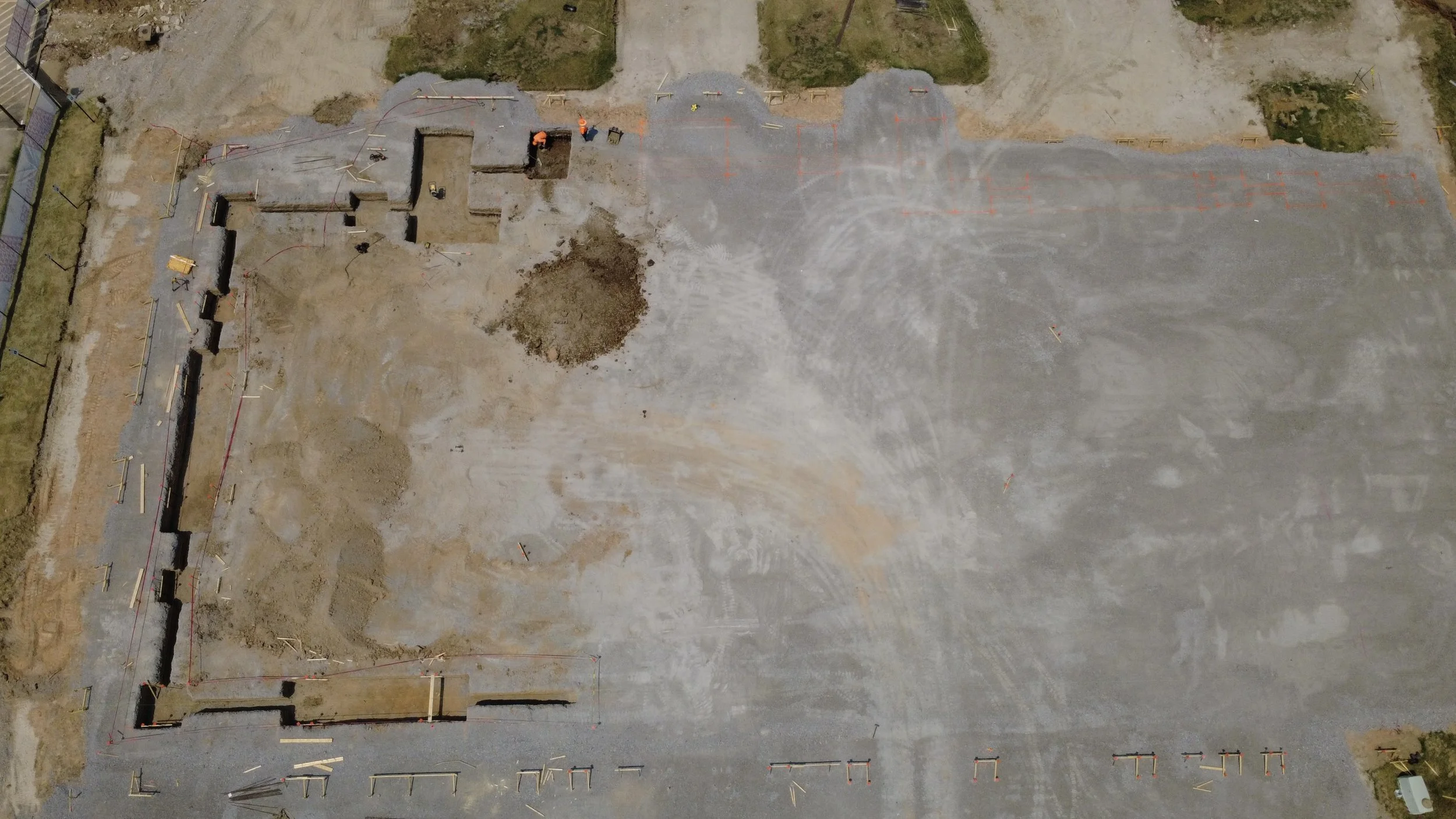 An aerial view of a construction site showing partially built concrete structures, construction workers, and grading areas with dirt and gravel.