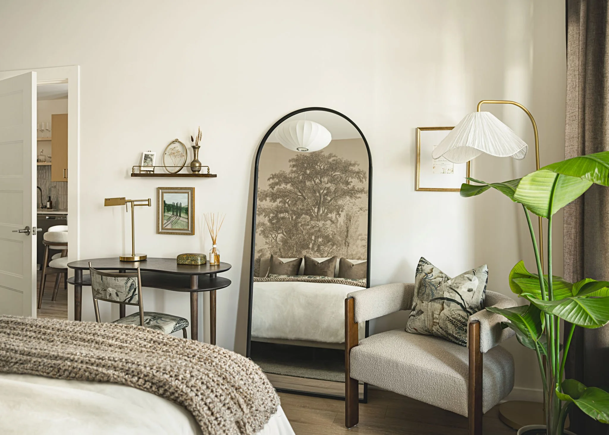 Interior of a stylish living room with beige walls, a large mirror, comfortable chairs, green plants, and decorative items.