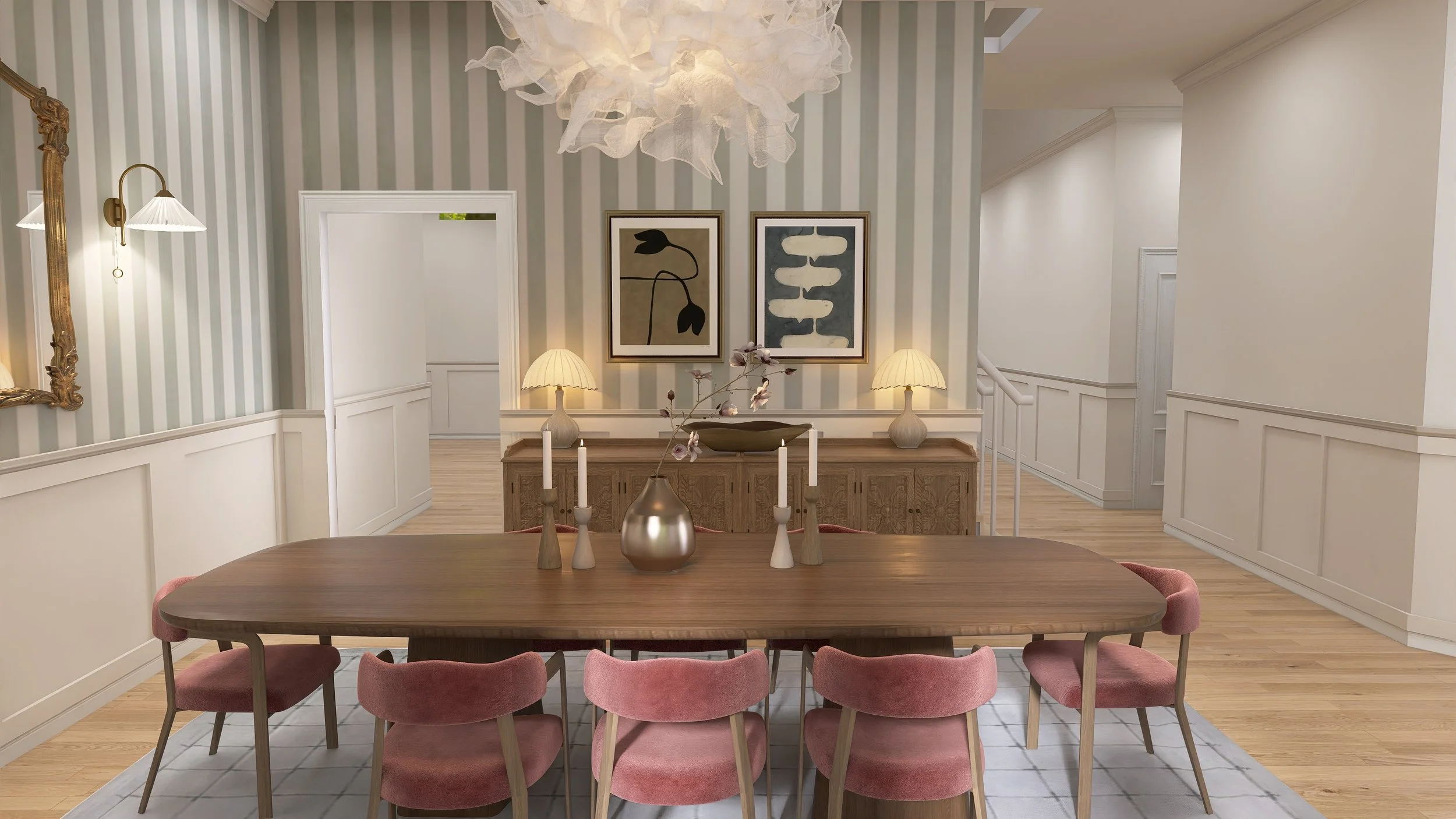 A dining room with a wooden table surrounded by pink upholstered chairs. On the table are decorative vases and candles. The background features a sideboard with two lamps, framed artwork on the wall, and a large cloud-like light fixture hanging from 