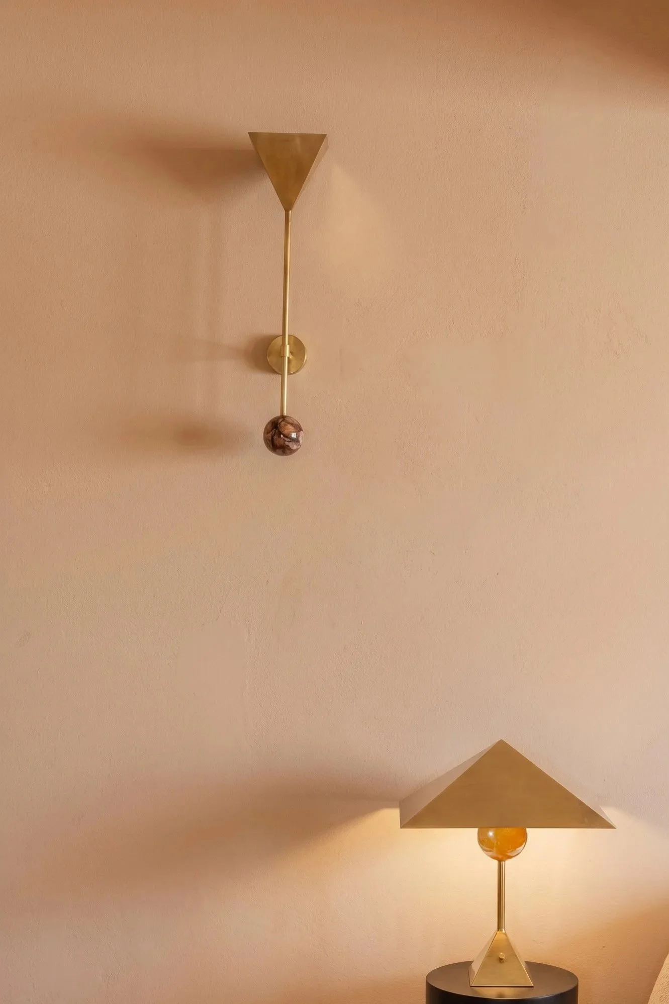 Modern decorative lamp with geometric shapes and metallic finishes, placed on a small round black table against a beige wall.
