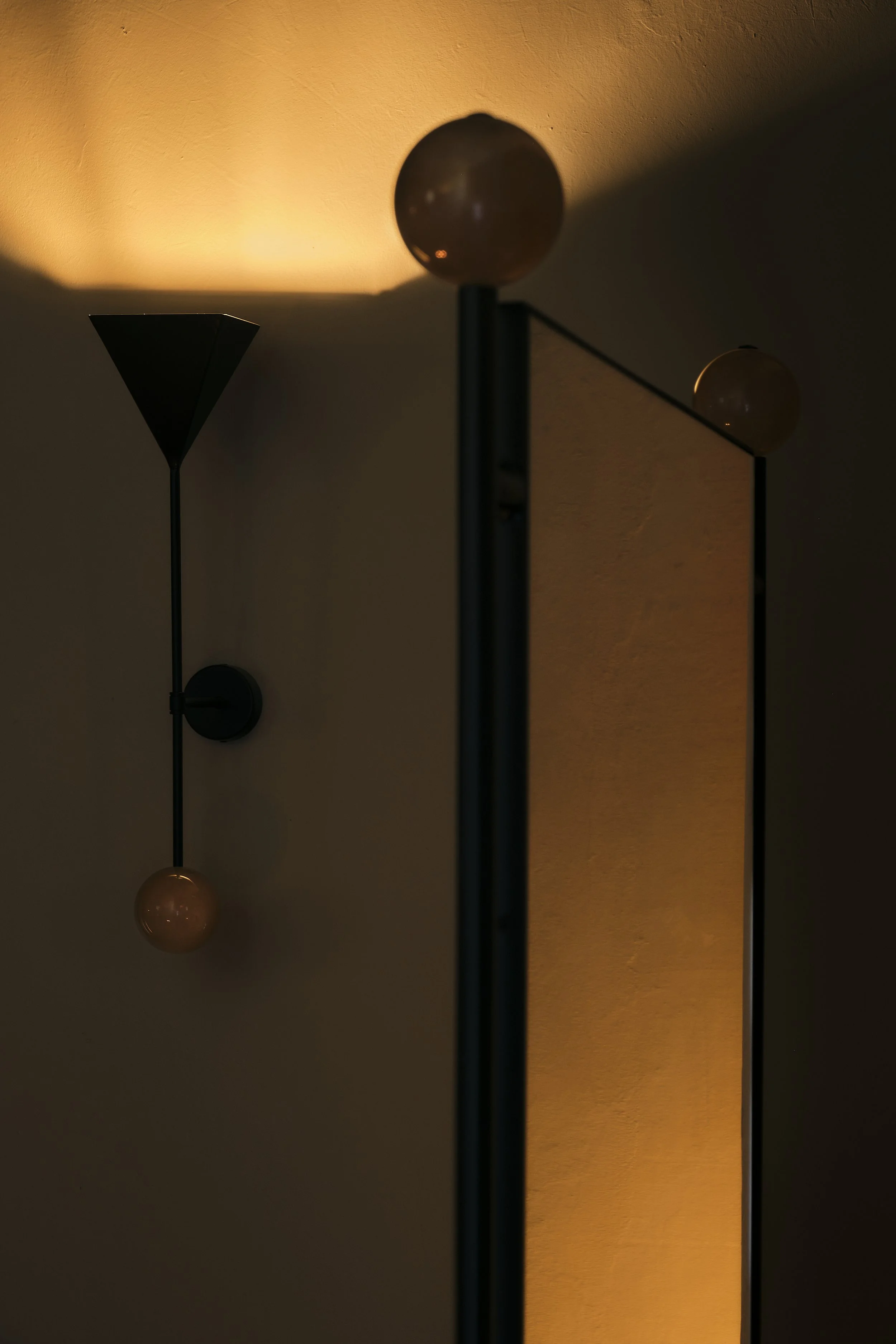 Close-up of a modern wall-mounted lamp with spherical bulbs against a warm, textured wall, creating a soft glow.