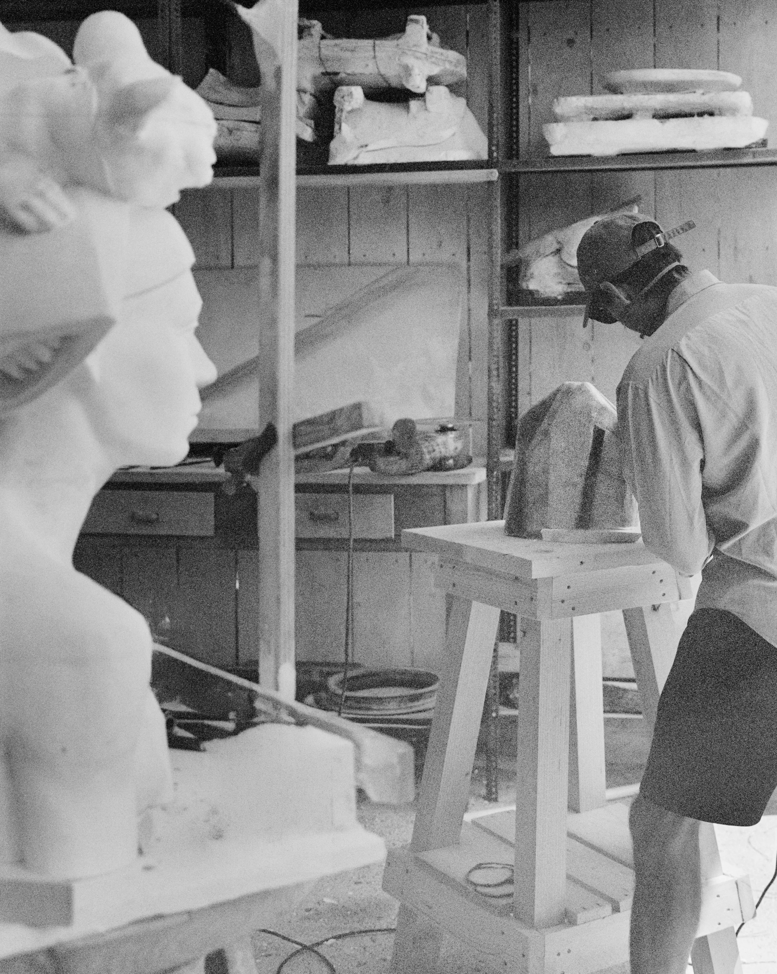 Men working with clay sculptures in a pottery studio, wearing masks and protective gear.
