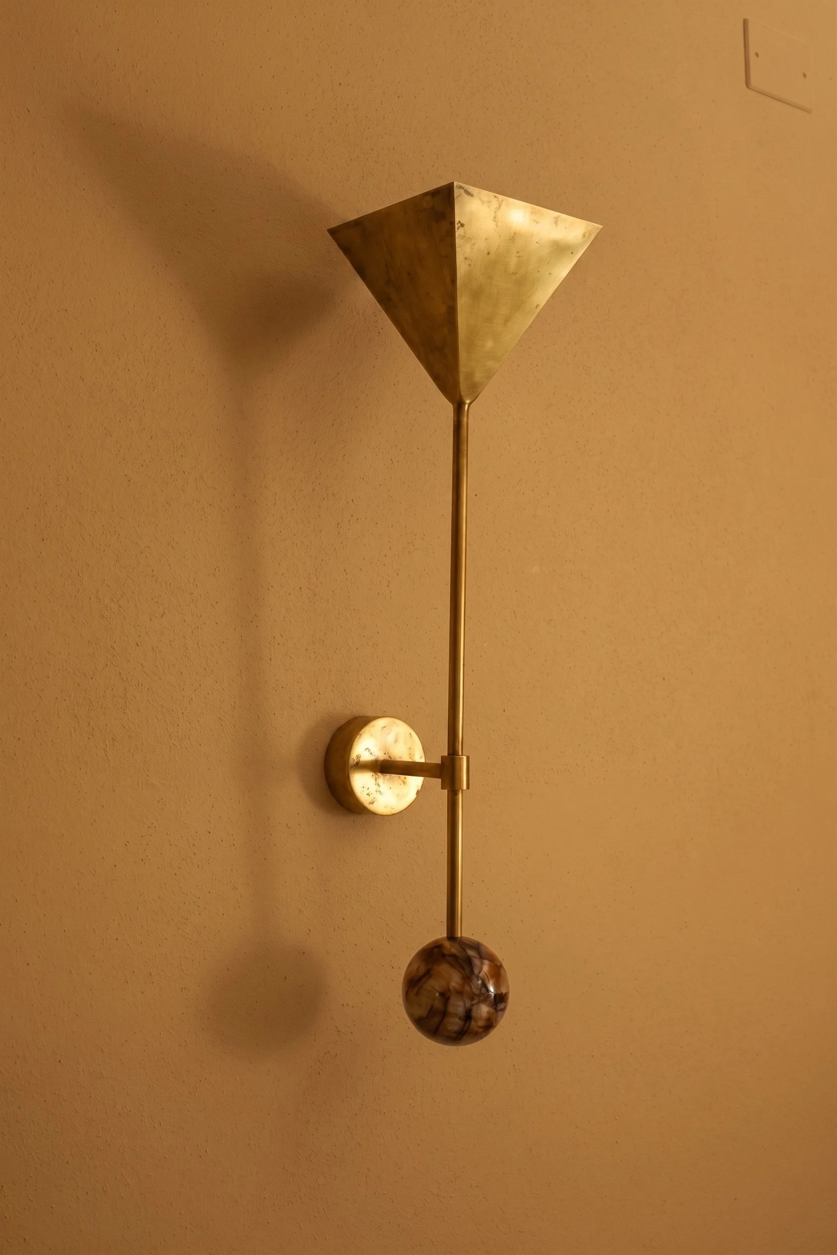 A modern wall-mounted light fixture with a metal shade and marble accents against a beige textured wall.