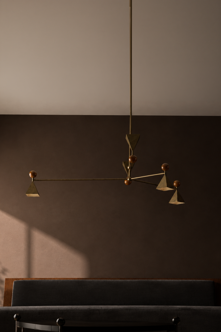 Modern geometric pendant light fixture hanging from the ceiling above a dark upholstered headboard in a bedroom.
