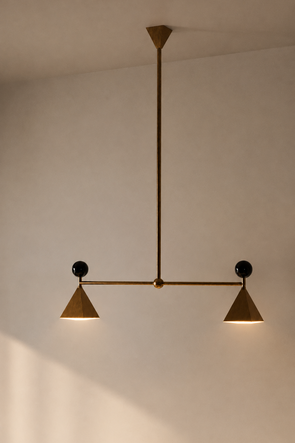 Modern ceiling light fixture with two cone-shaped shades and black spherical accents, suspended from a gold rod attached to the ceiling.