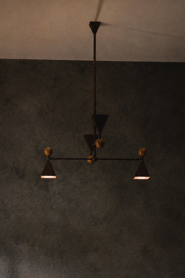 Modern ceiling chandelier with black metal arms and wood spherical accents, hanging in a room with dark walls and ceiling.