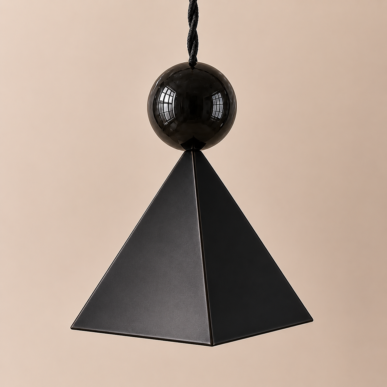 A geometric decor piece featuring a black pyramid-shaped base with a black sphere on top, suspended by a black cord, against a beige background.