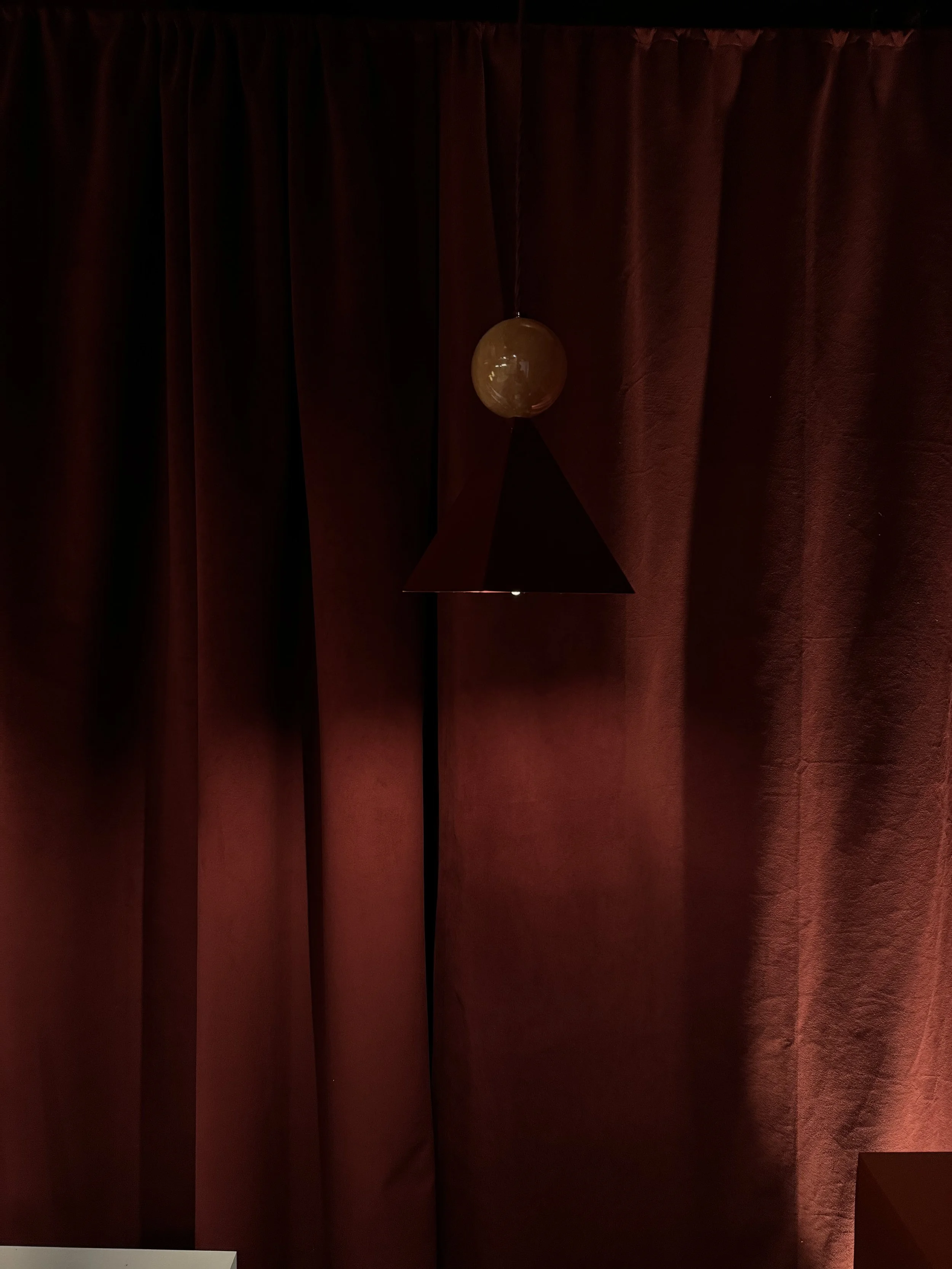 A dark red curtain with a pendant light hanging in front of it.