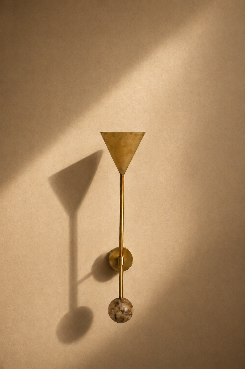 Wall-mounted light fixture with a cone-shaped shade, a vertical rod, and a spherical element at the bottom, casting shadows on a beige wall.