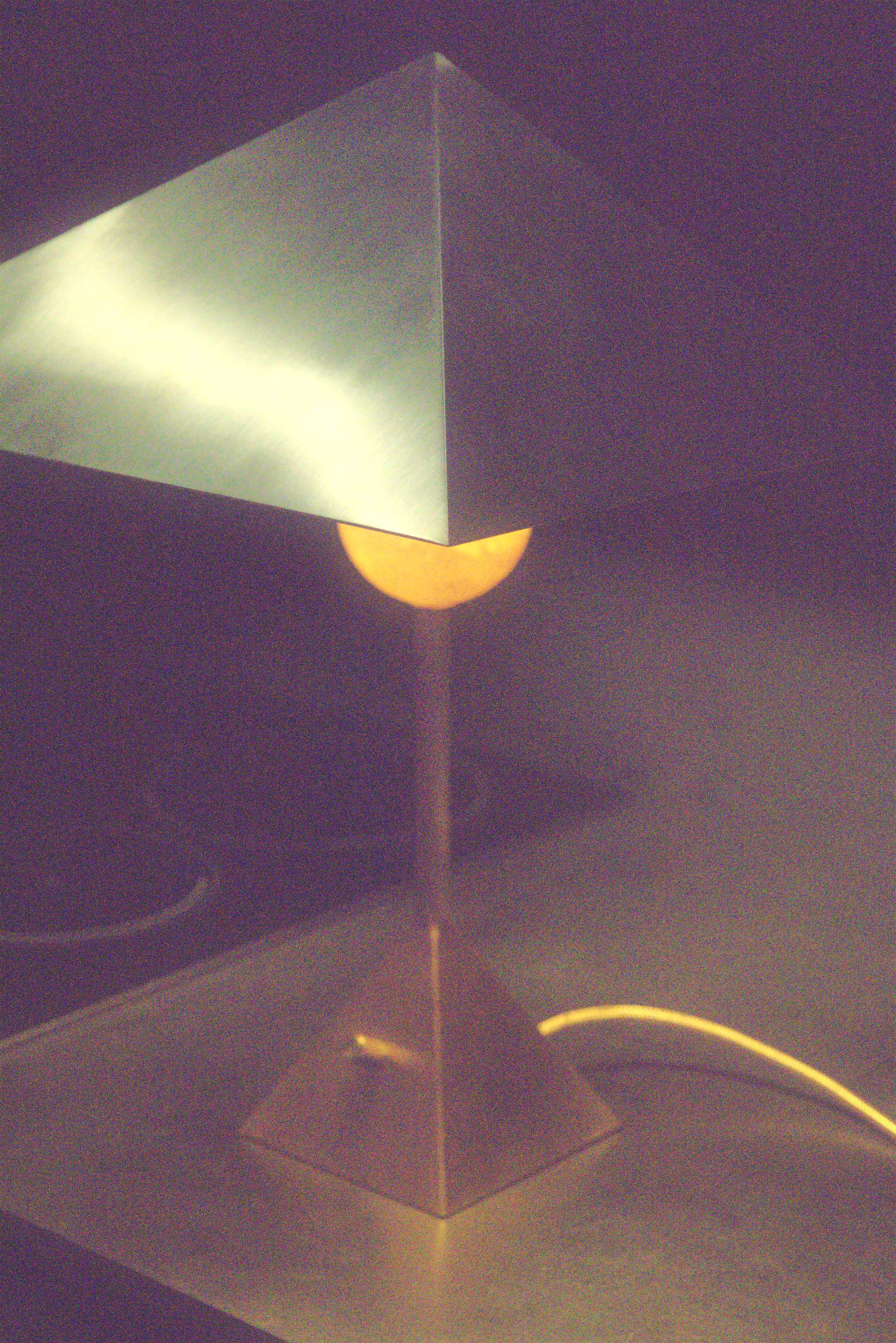 A geometric lamp with a cube-shaped frame and a semi-sphere at the bottom, emitting soft light, placed on a table in a dimly lit room.