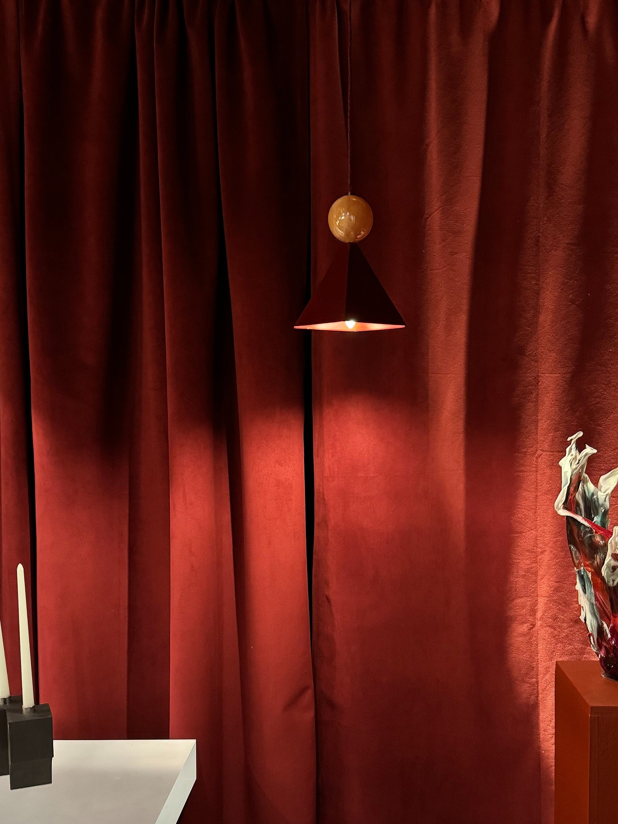 A hanging pendant lamp with a round, marble-like globe above a conical shade, against a backdrop of red velvet curtains.