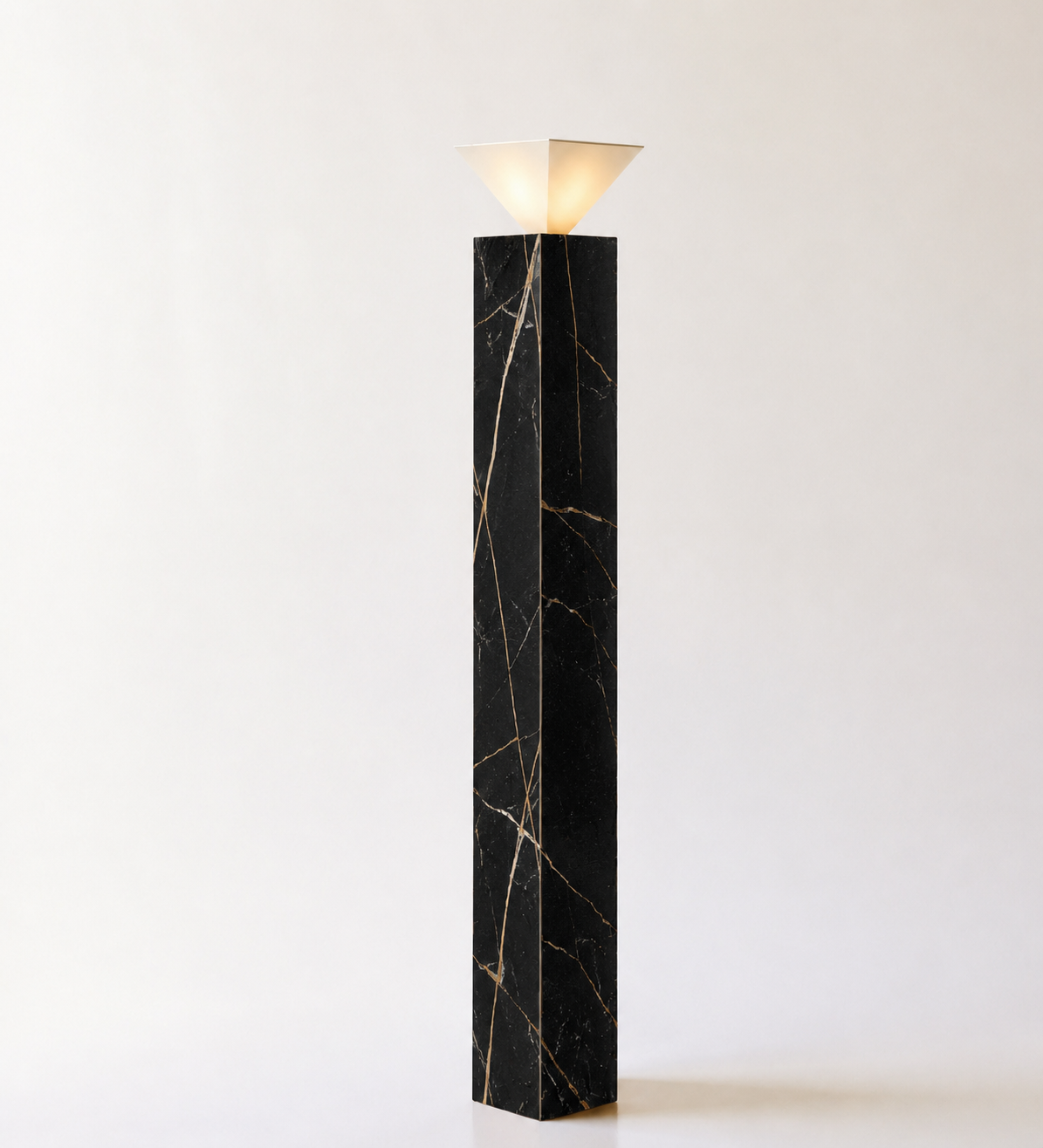 A modern black marble floor lamp with gold veins, featuring a geometric beige lampshade on top, set against a plain light-colored background.