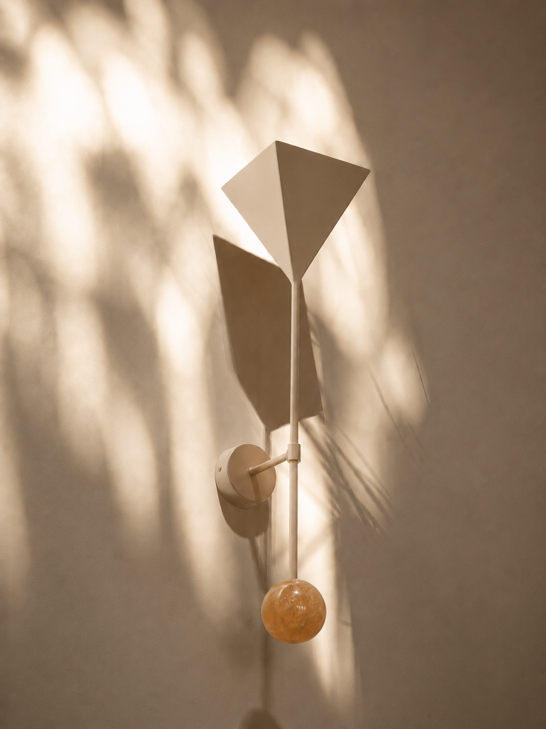 A modern wall sconce with an abstract geometric design, casting patterned shadows on a beige wall.