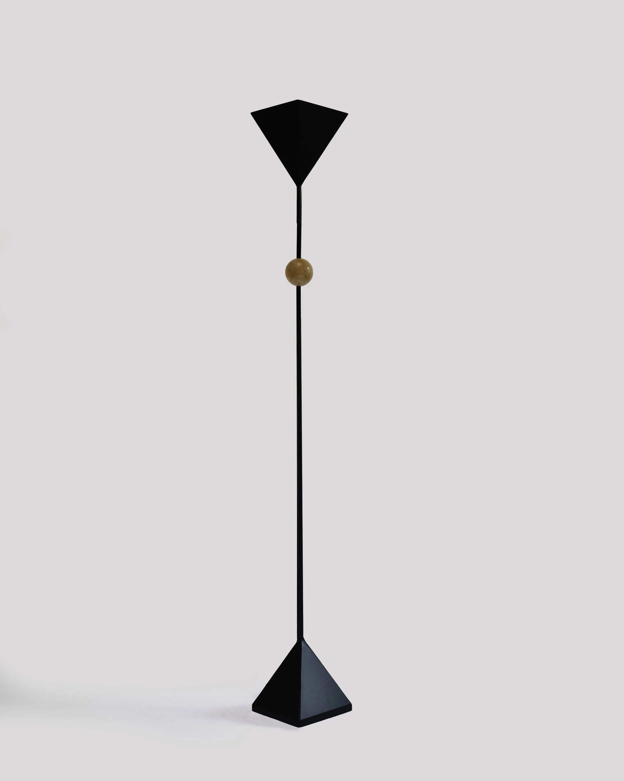 Modern sculpture with black geometric shapes connected by a thin black rod and a small wooden bead, set against a plain light gray background.