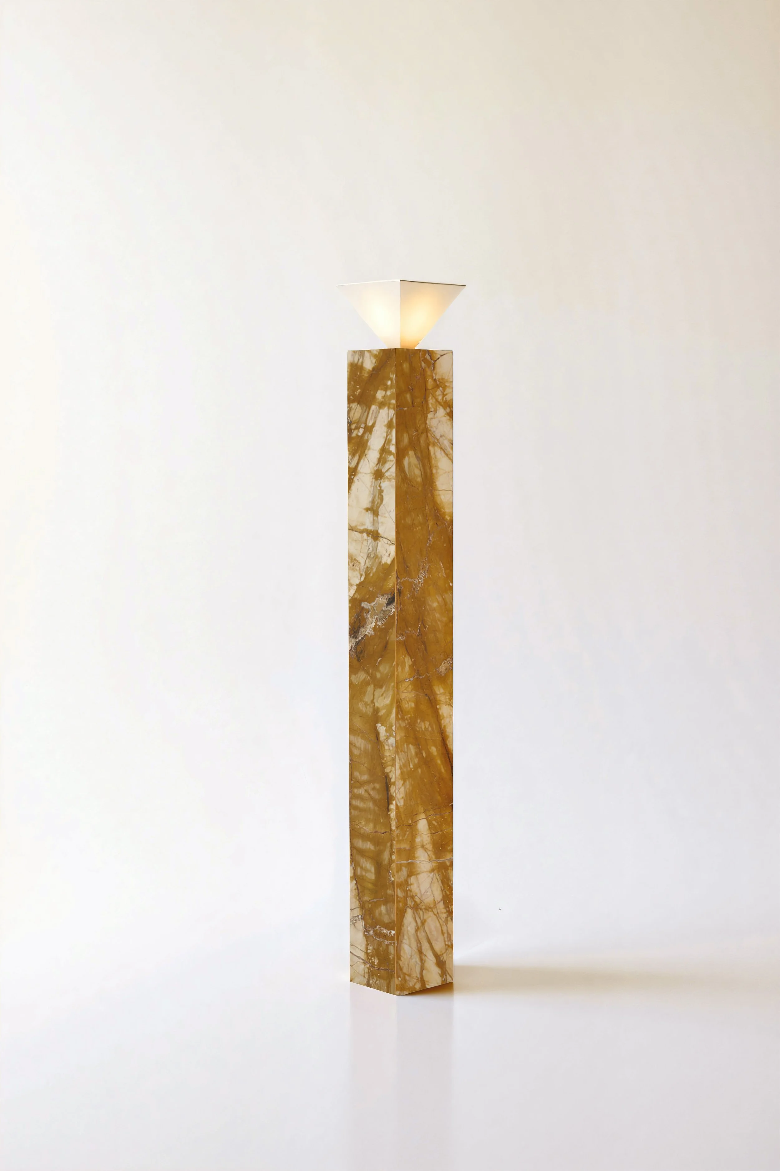 A tall marble pedestal with brown and cream veining, topped with a white geometric-shaped lampshade, against a plain white wall.