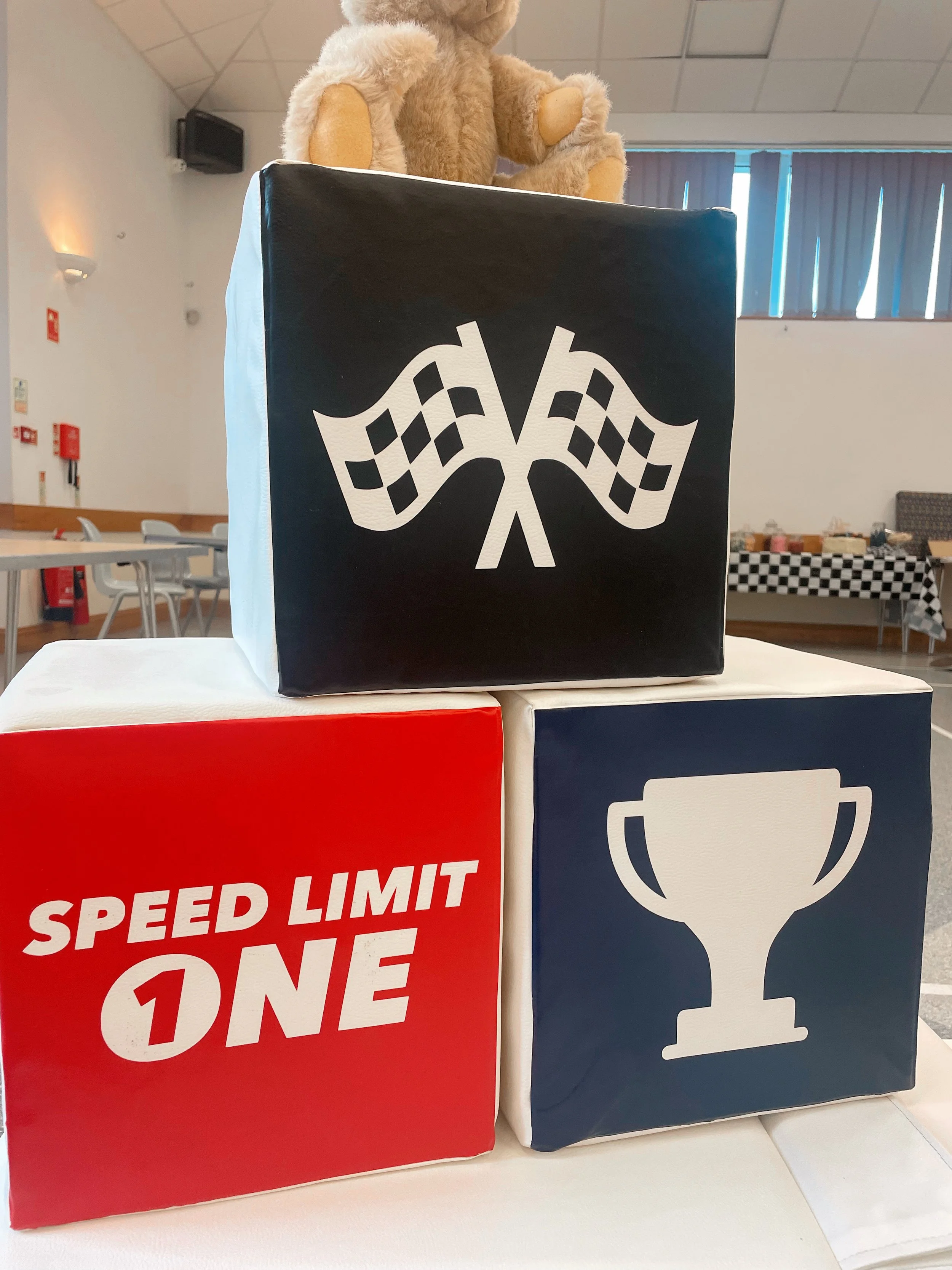 Three stacked blocks with racing-themed designs, topped with a teddy bear.