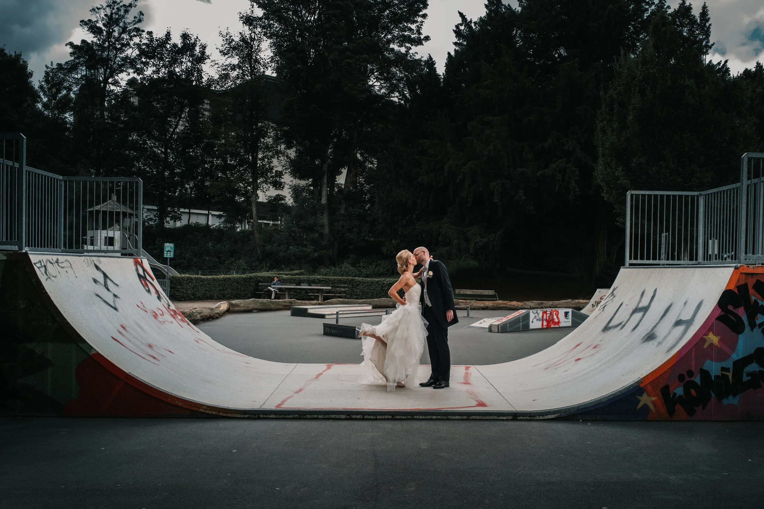 Ein Brautpaar in Hochzeitskleidung im Skatepark, das sich küsst.
