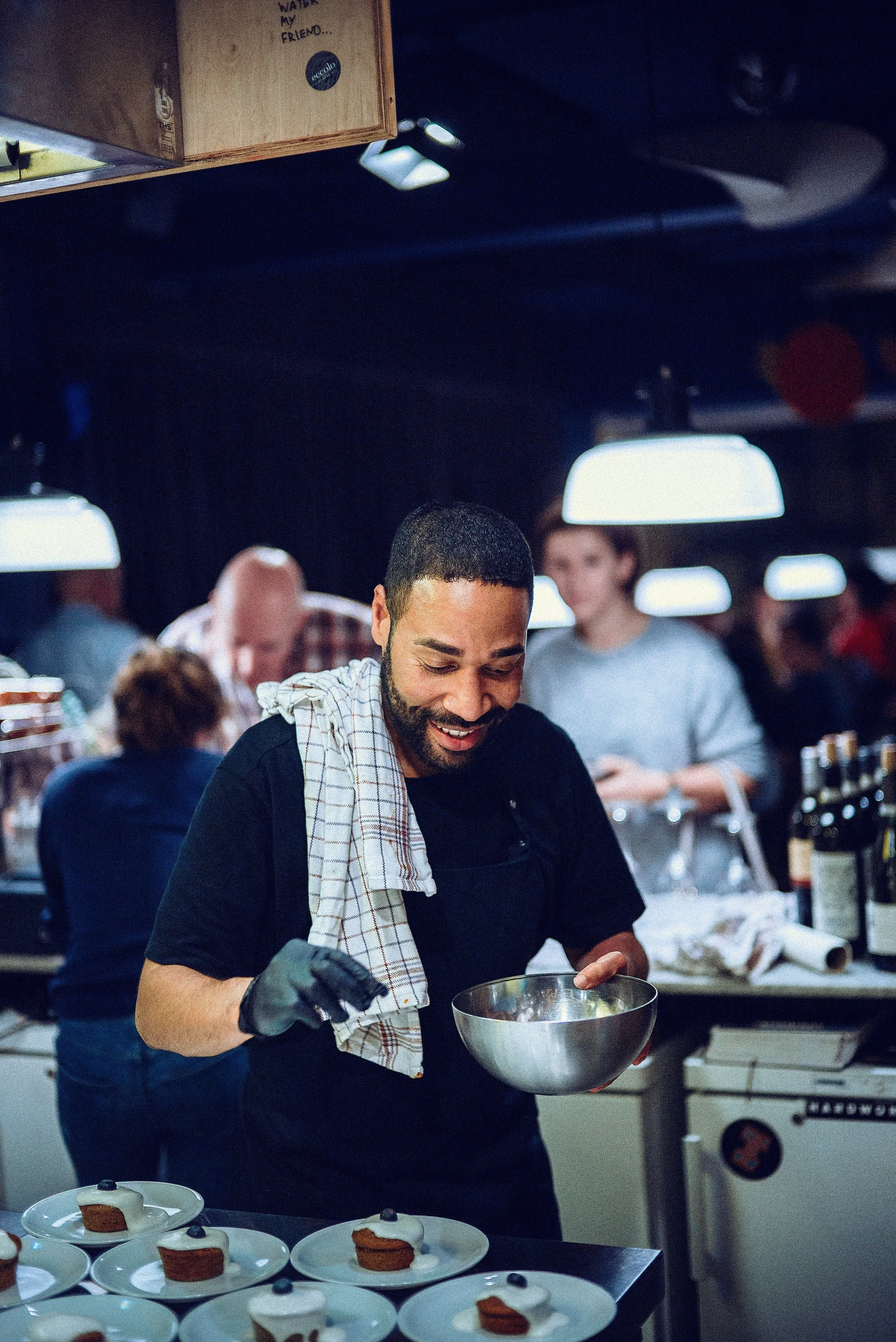 Ein Mann in einer Restaurantküche bereitet Kuchen vor, auf dem Tisch liegen kleine Kuchen mit Creme und Beeren.