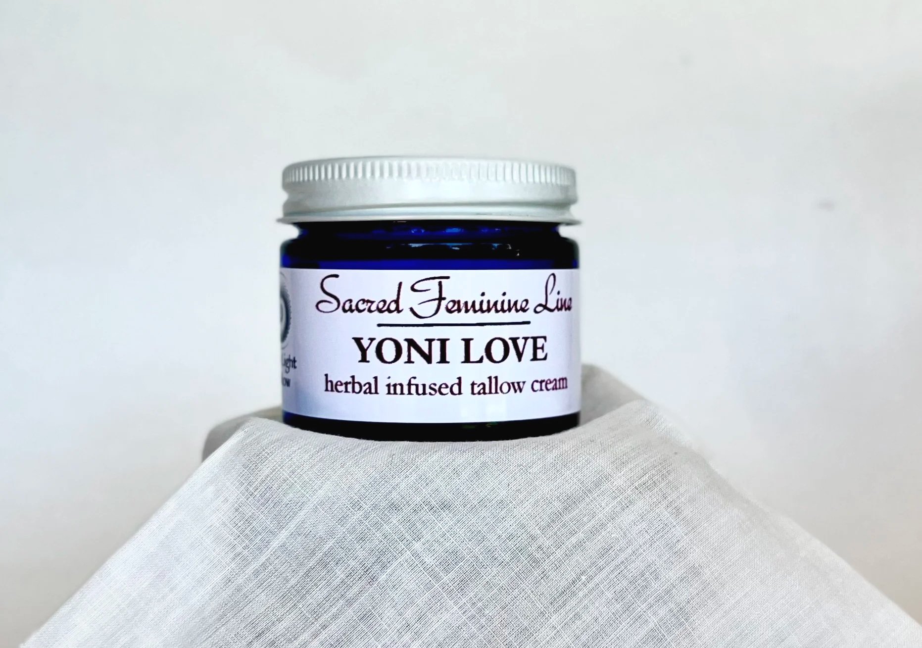 Small dark blue jar of Sacred Feminine Lime Yoni Love herbal infused tallow cream on a white cloth surface