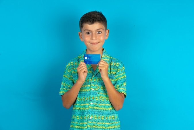Boy in blue and green shirt holding a debit card.