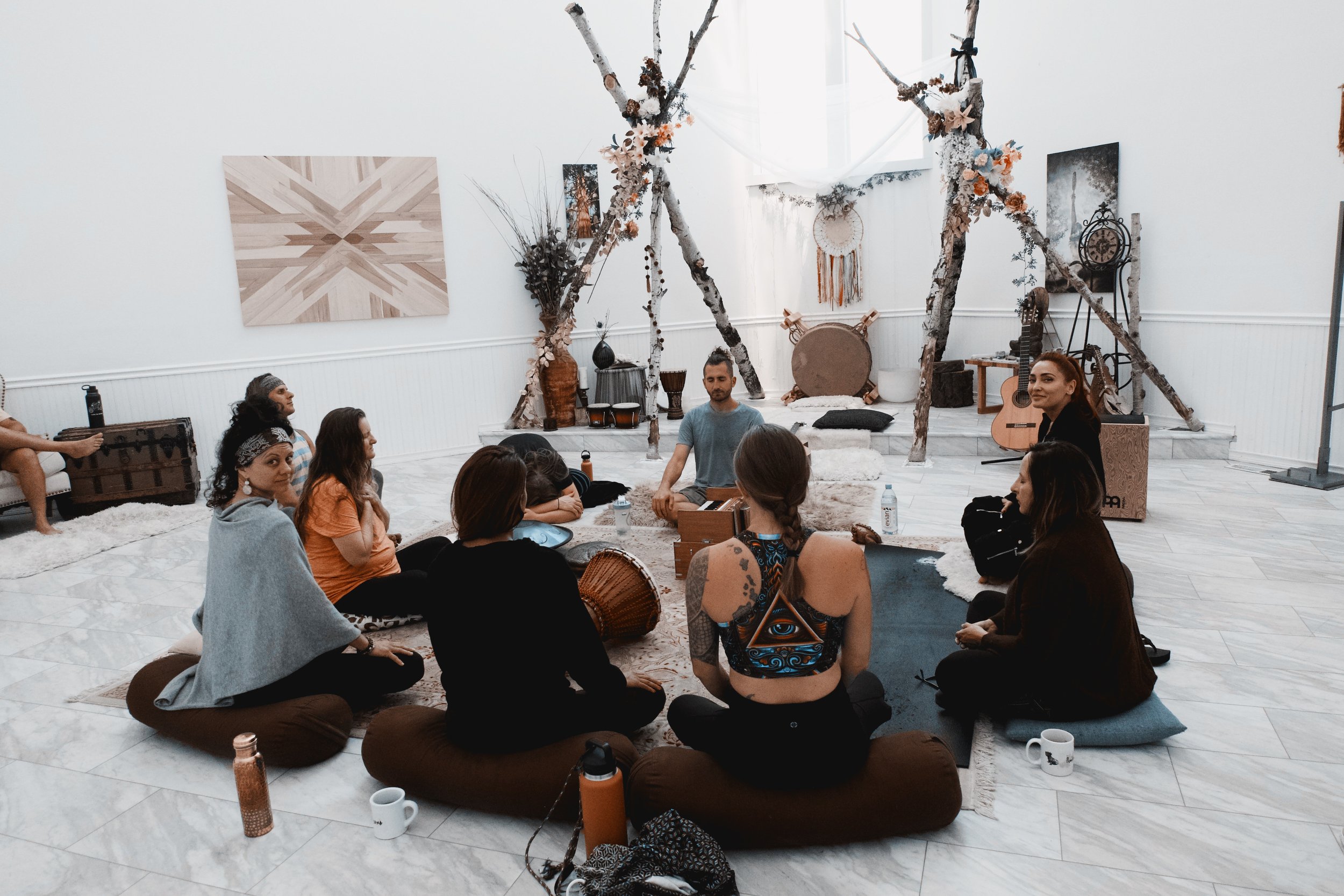 Group meditation session in a decorated indoor space with wooden decor and cushions.