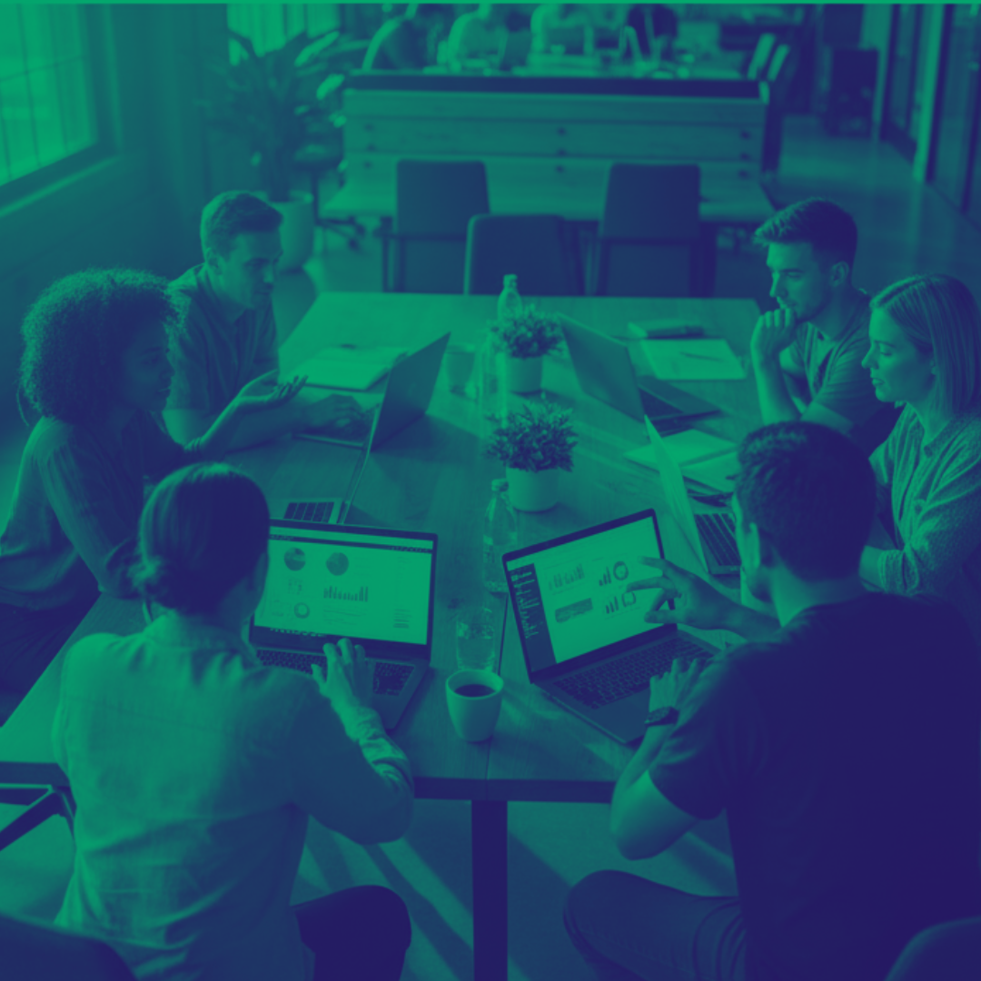 A group of six young adults sitting around a wooden table in a modern office, collaborating on laptops and discussing documents.