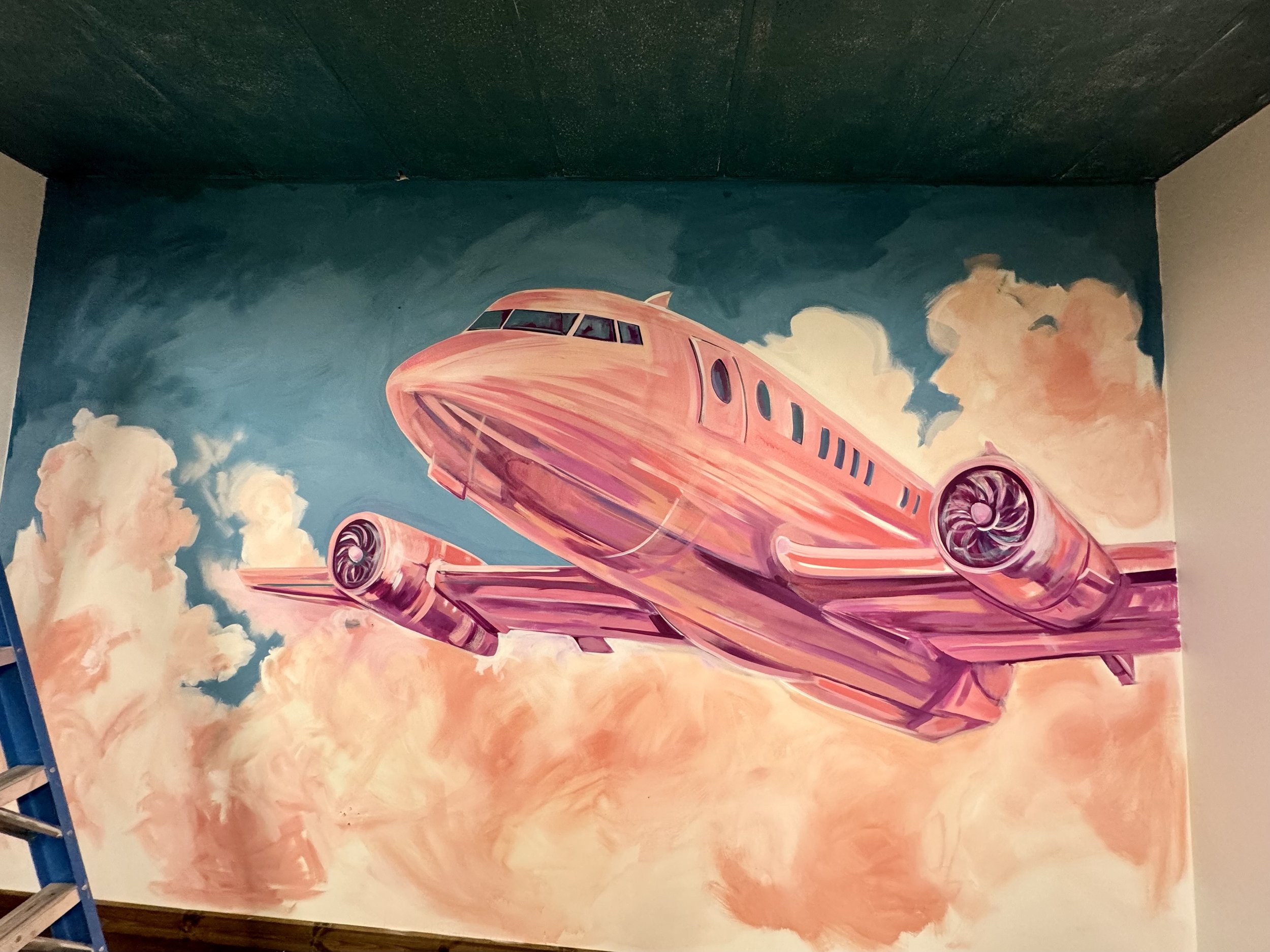 Mural of airplane in pink surrounded by clouds and blue sky