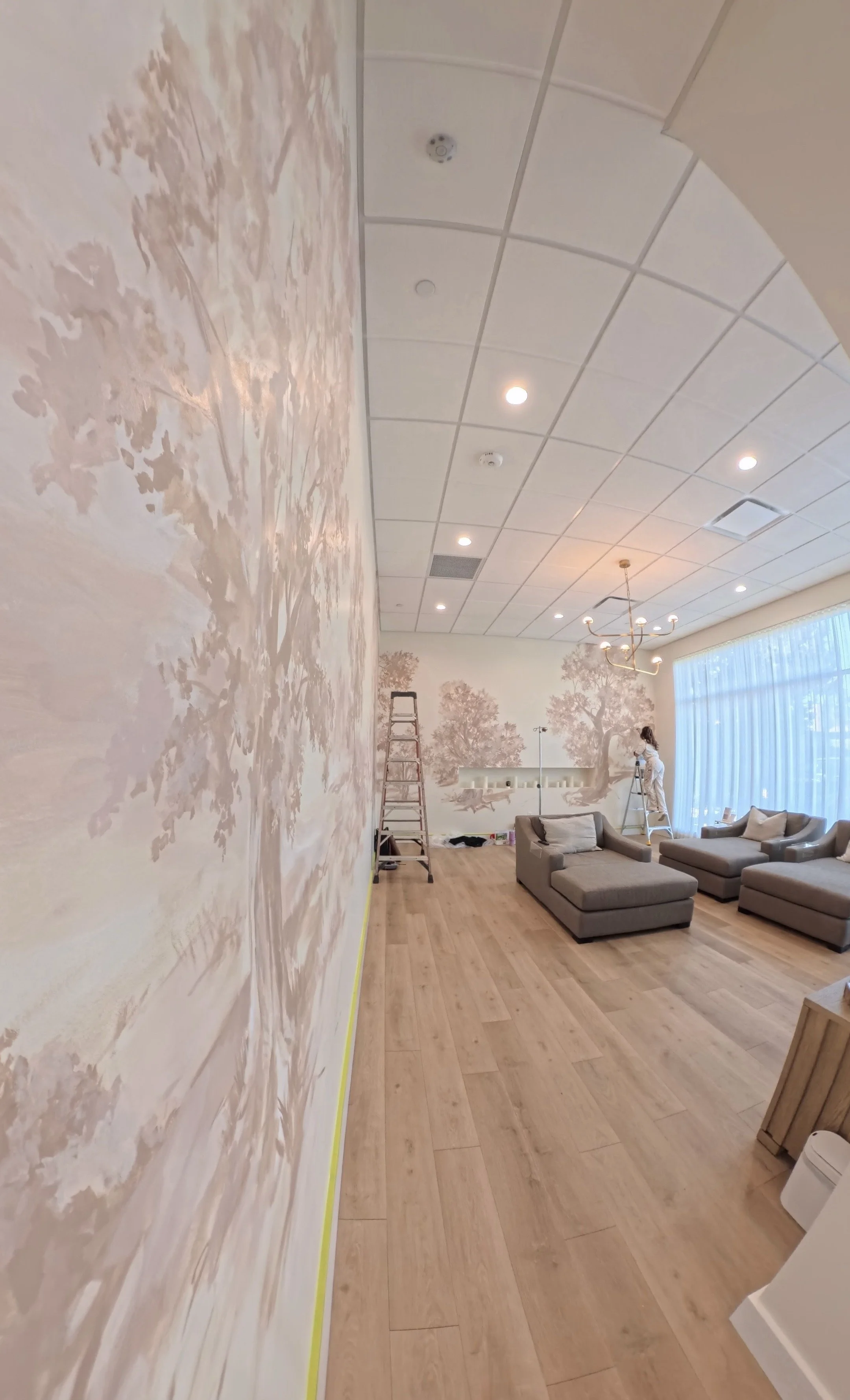 Elysia painting a mural on a wall of pink trees