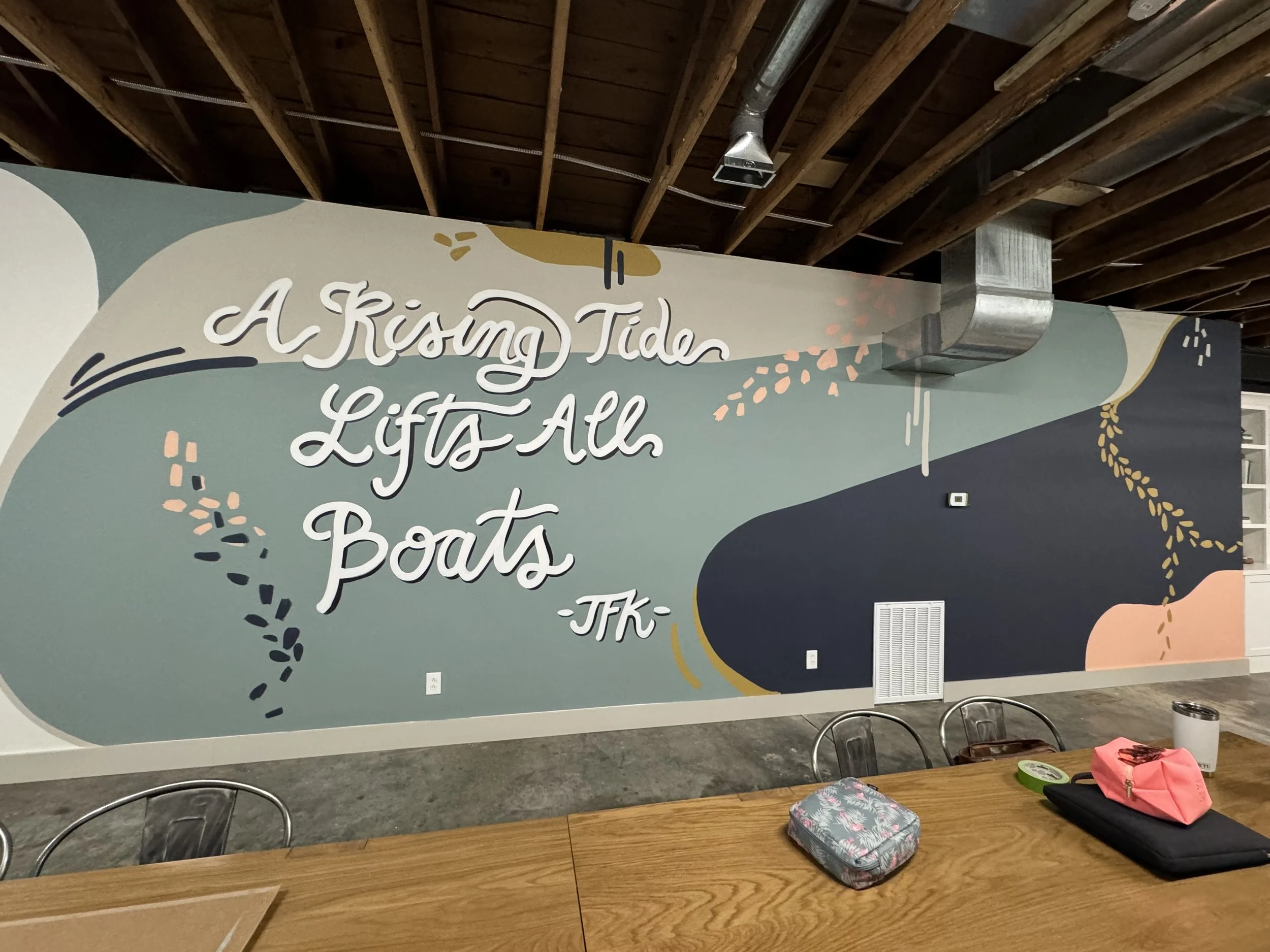 Mural with organic shapes and a hand lettered quote that reads "A Rising Tide Lifts All Boats – JFK"
