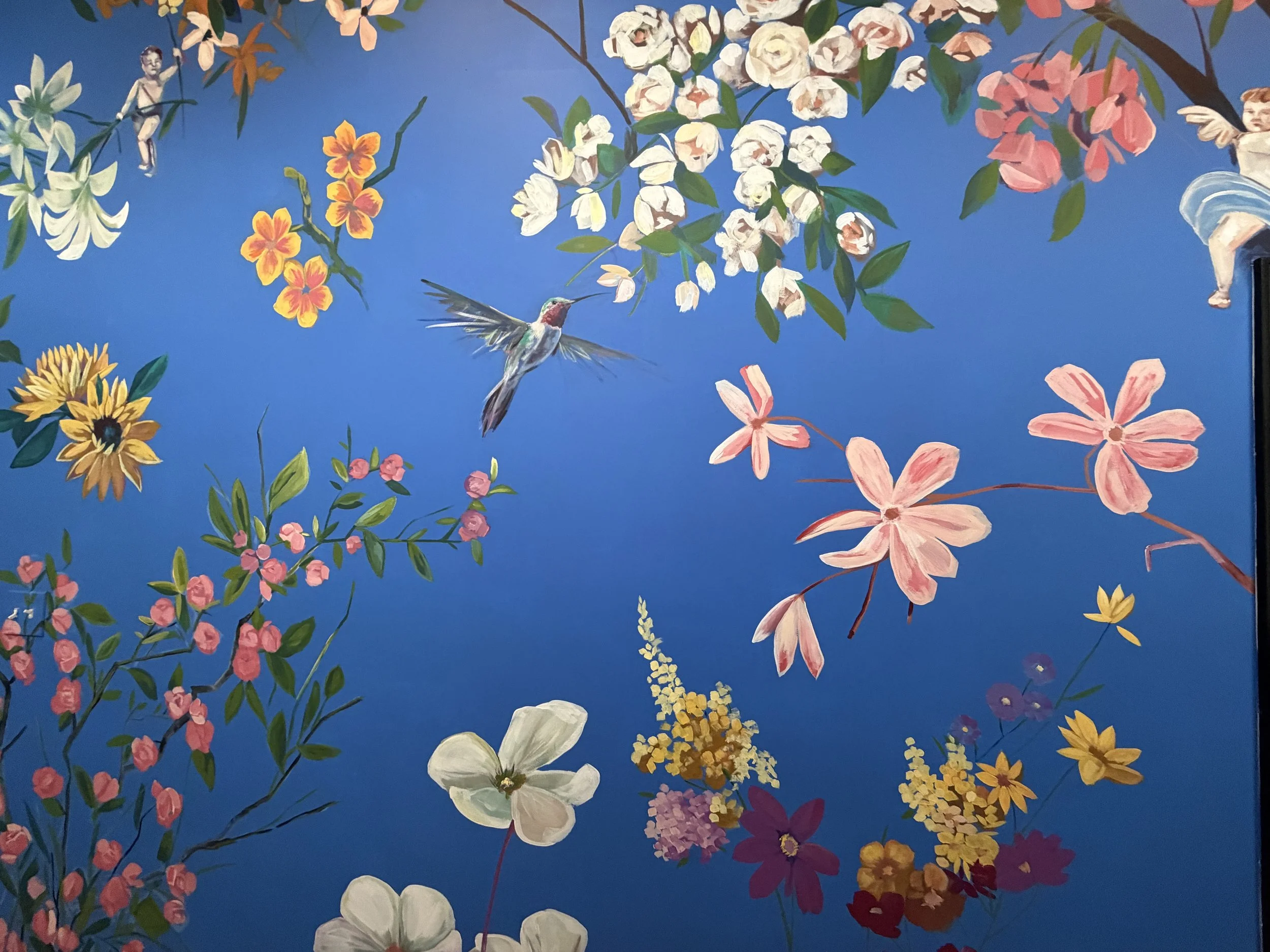 Mural of a blue wall with flowers and a hummingbird