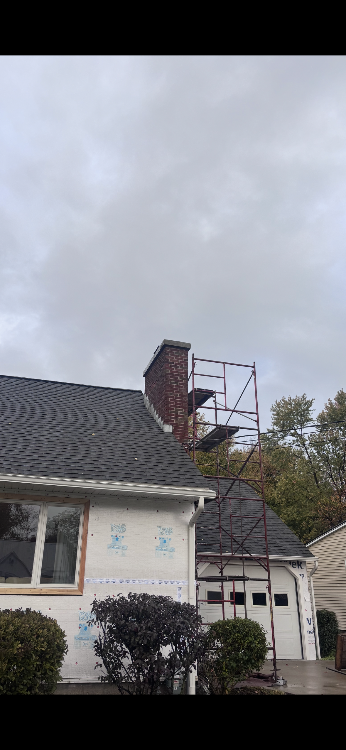 Scaffolding set up next to a house with a brick chimney under a cloudy sky.