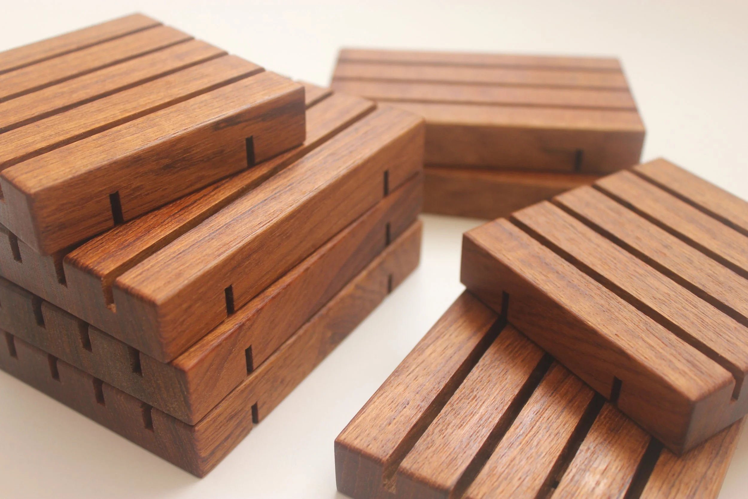 A stack of teak soap trays in square and standard sizes against a white background.
