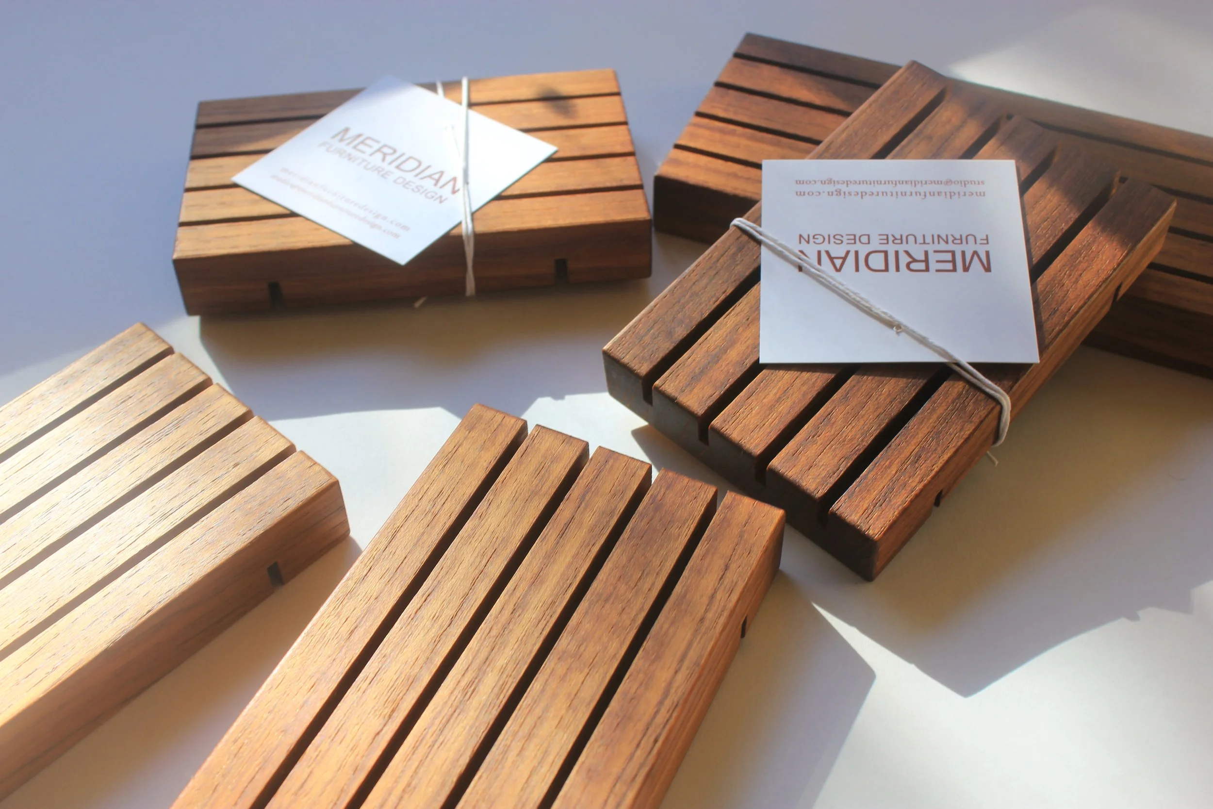 teak wooden soap trays in assorted sizes shown unwrapped alongside some in packaging with Meridian Furniture Design logo in red text on white label..jpg