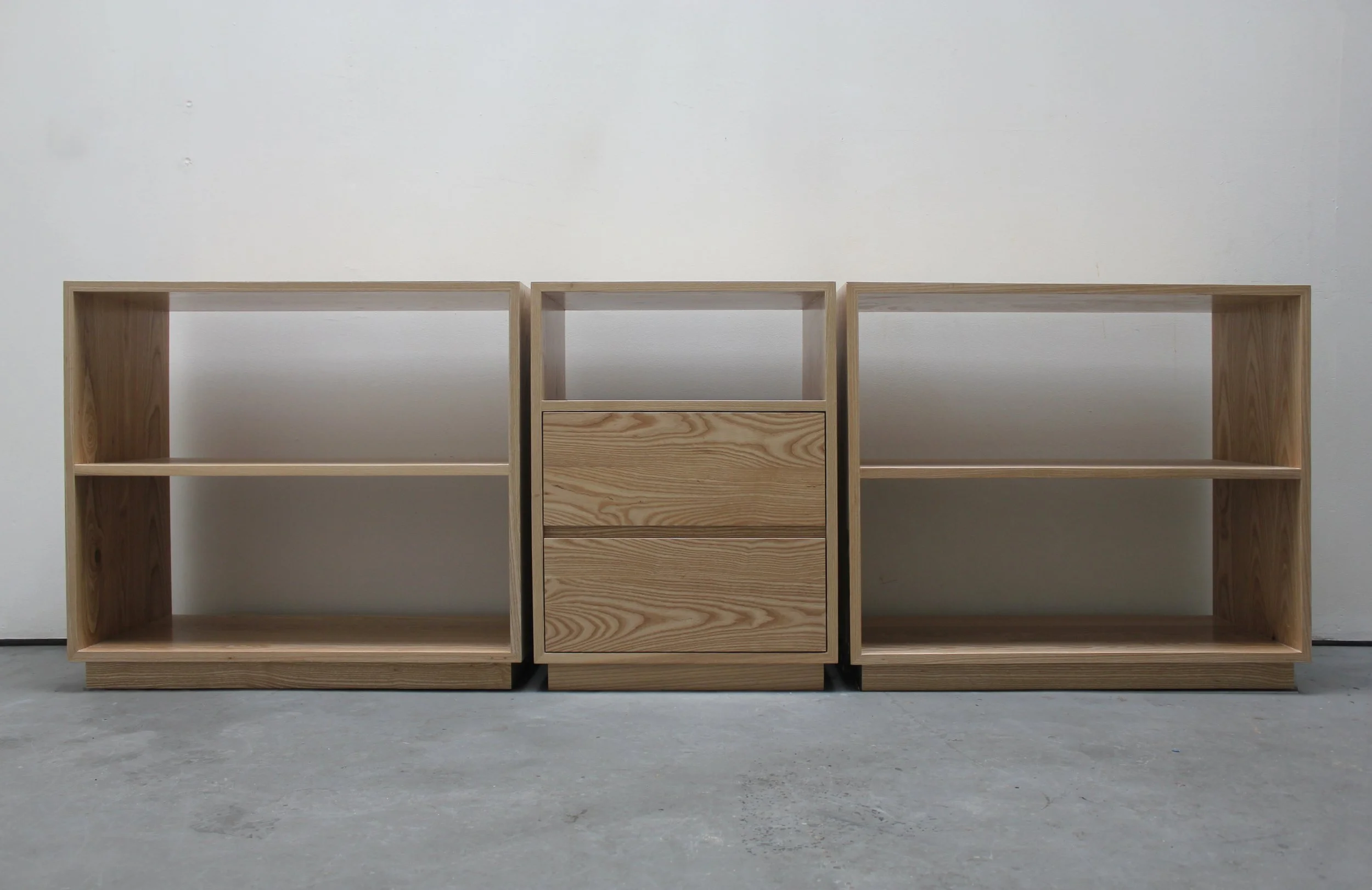 Open credenza composed of three separate cabinets with shelving, the center cabinet also has two drawers. Cabinets are made of a light colored ash wood with a natural finish.