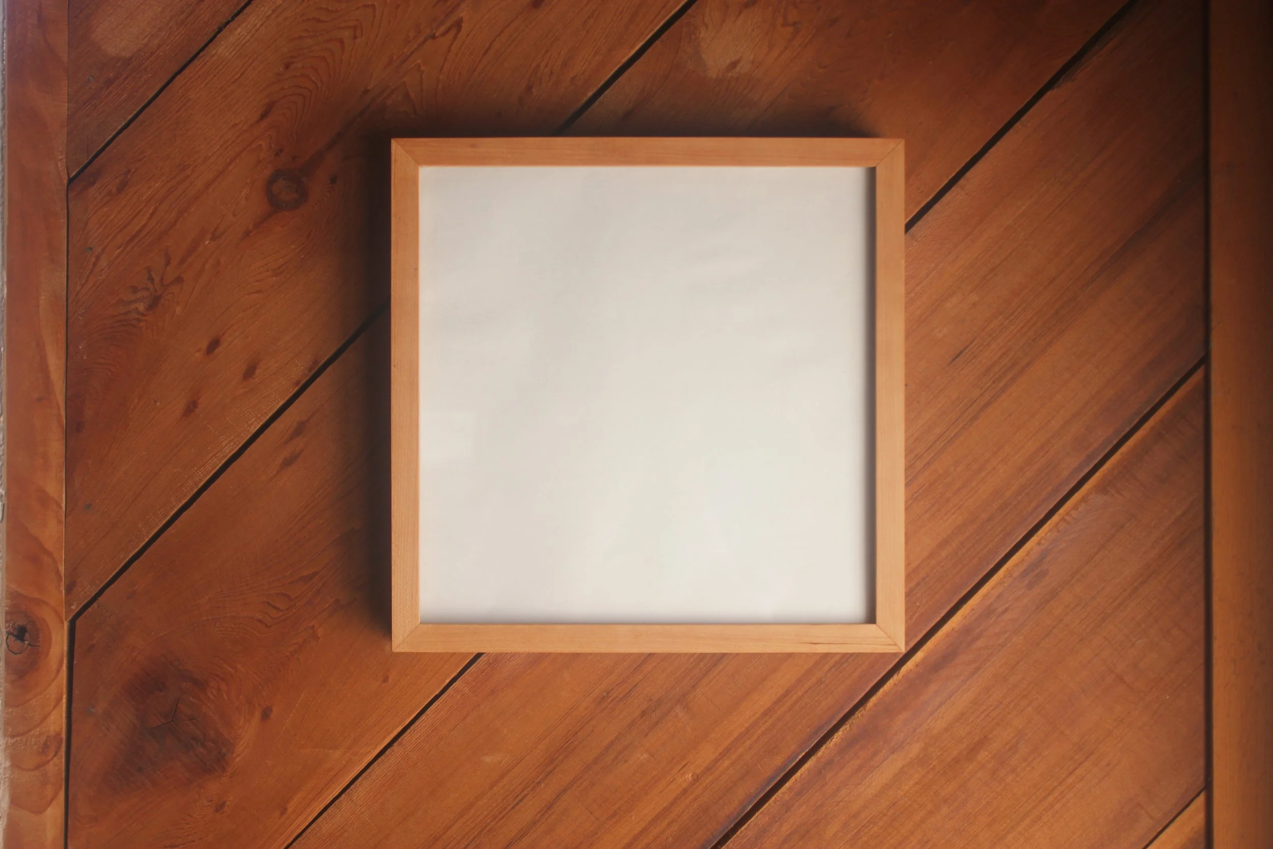 Gallery frame made of cherry wood shown hanging against a wooden wall.