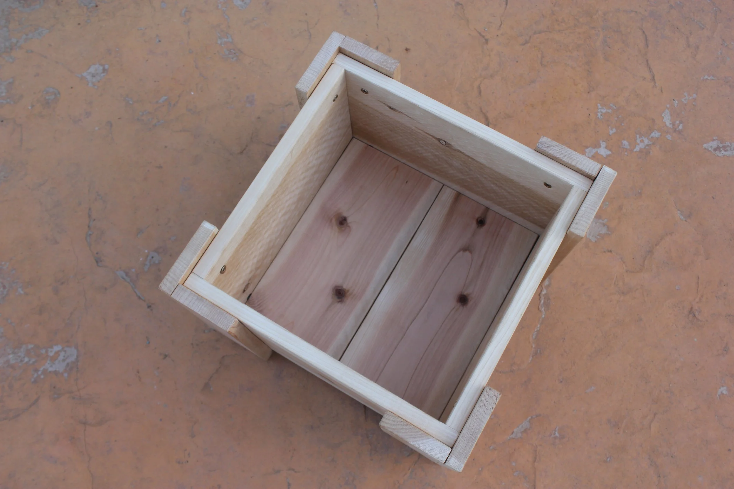 Detail of the interior of a cedar mini planter box against a patio background.