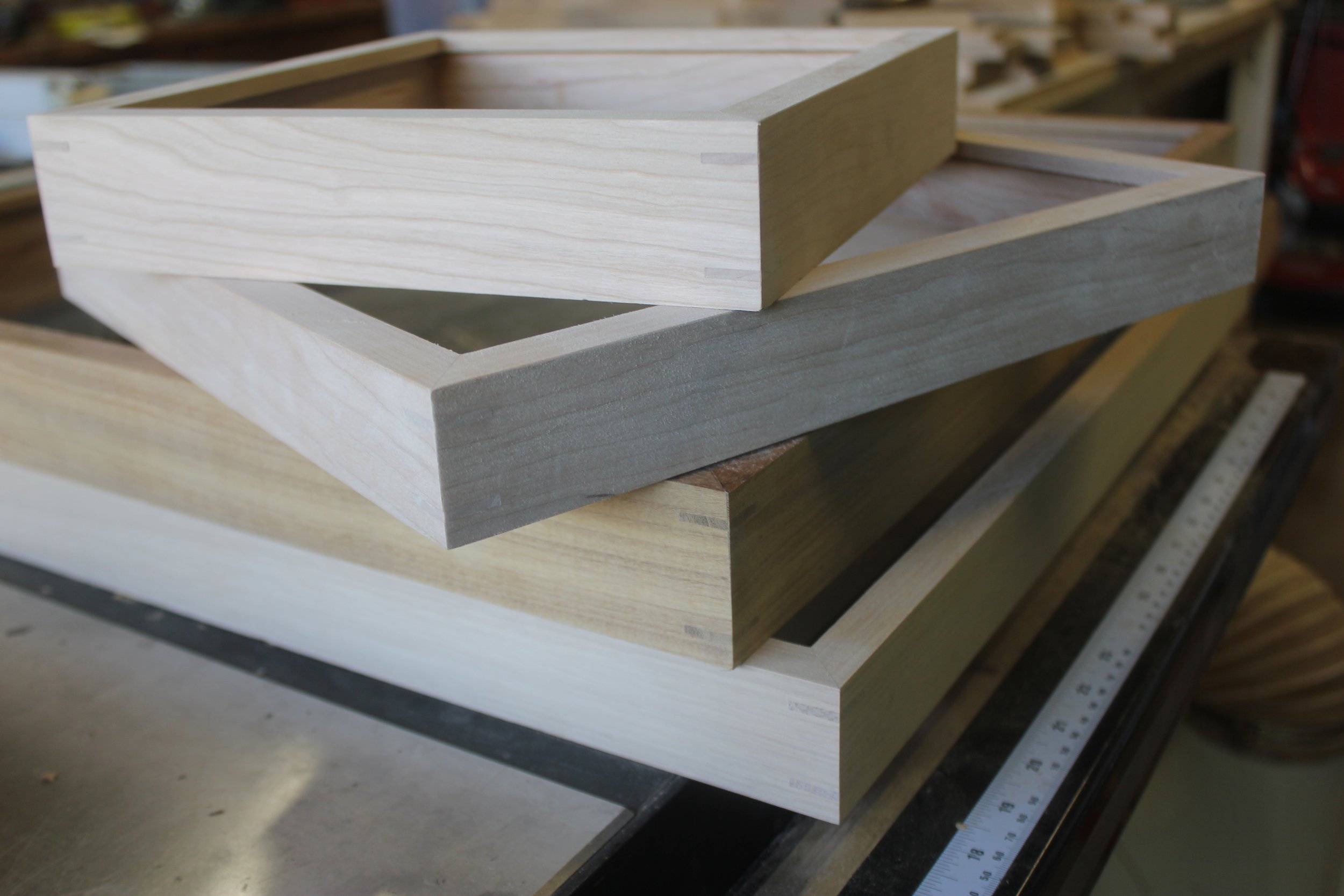 A stack of gallery frames in progress, shown in a wood shop setting. Frames are handmade in southern California from sustainably sourced domestic and FSC certified imported hardwoods.